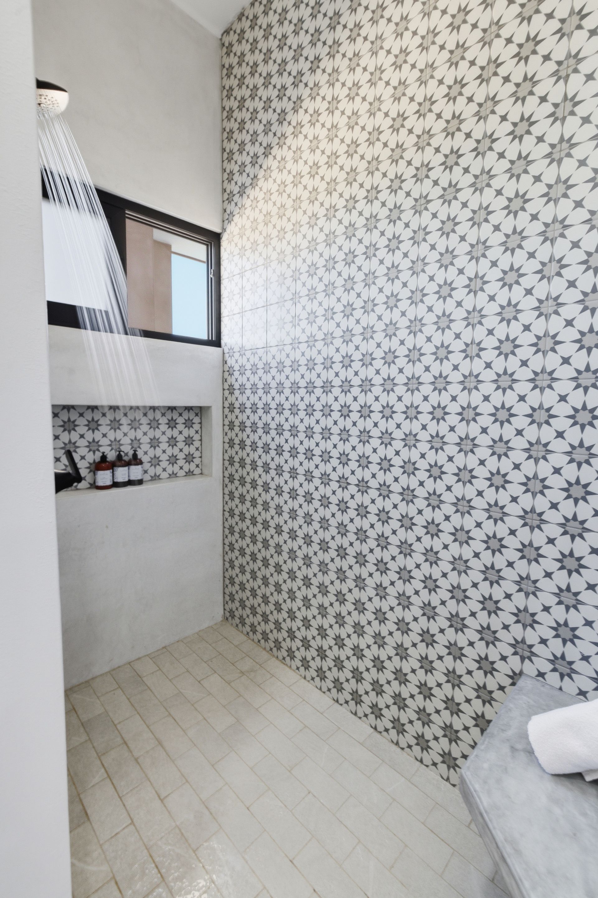 Shower with patterned star tiles, a window, and built-in shelf holding toiletries. Water streams from a showerhead.