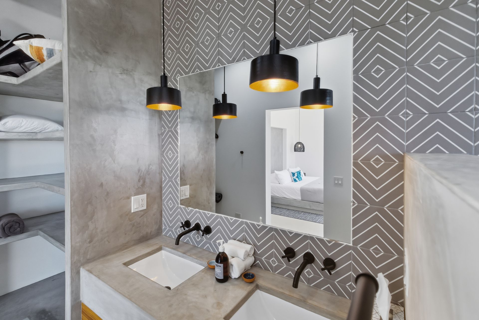 Bathroom with concrete countertop, patterned wallpaper, black pendant lights, and large mirror.