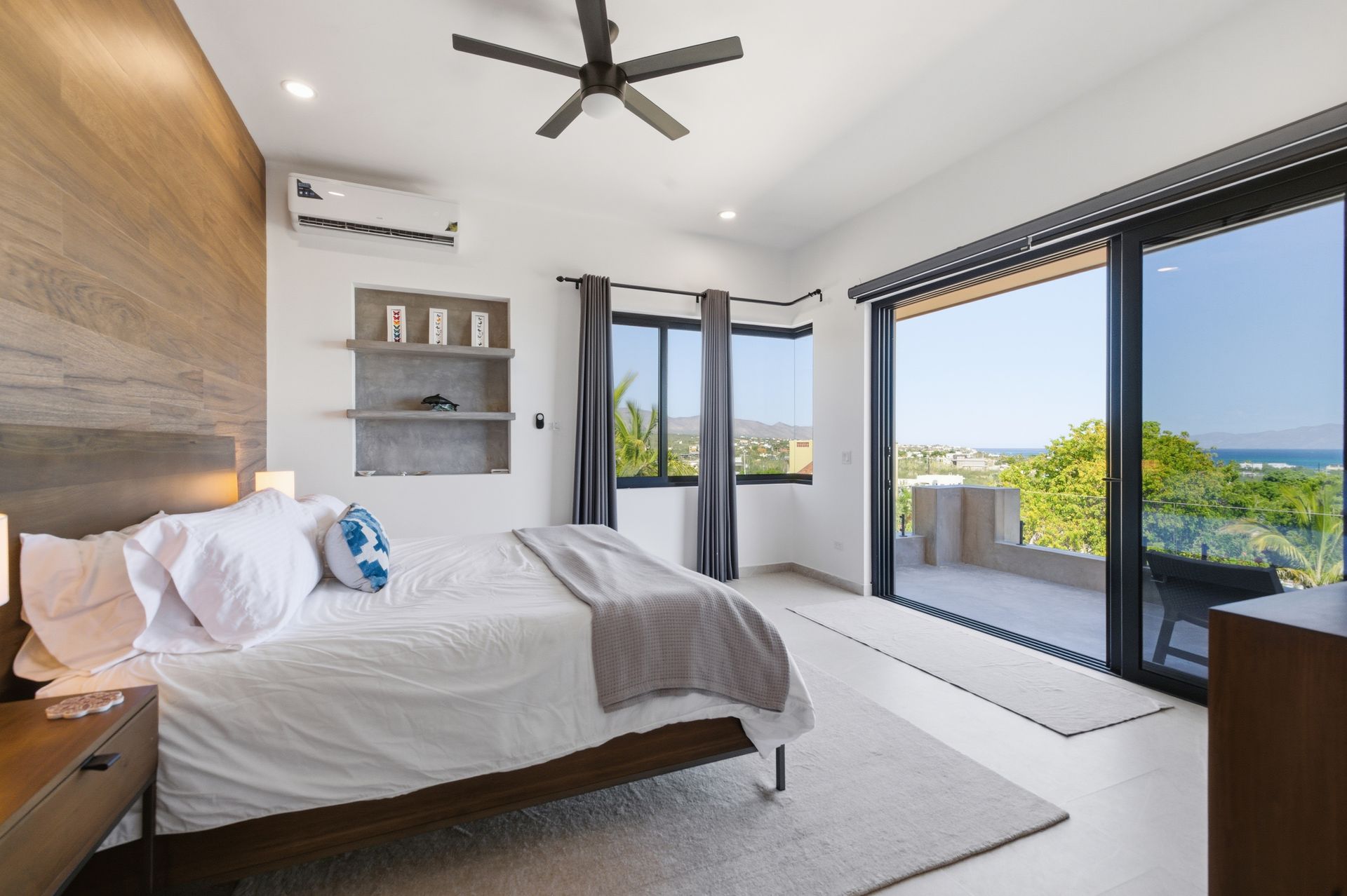 Bedroom with large bed, wooden accent wall, and sliding glass doors to a balcony overlooking the ocean.