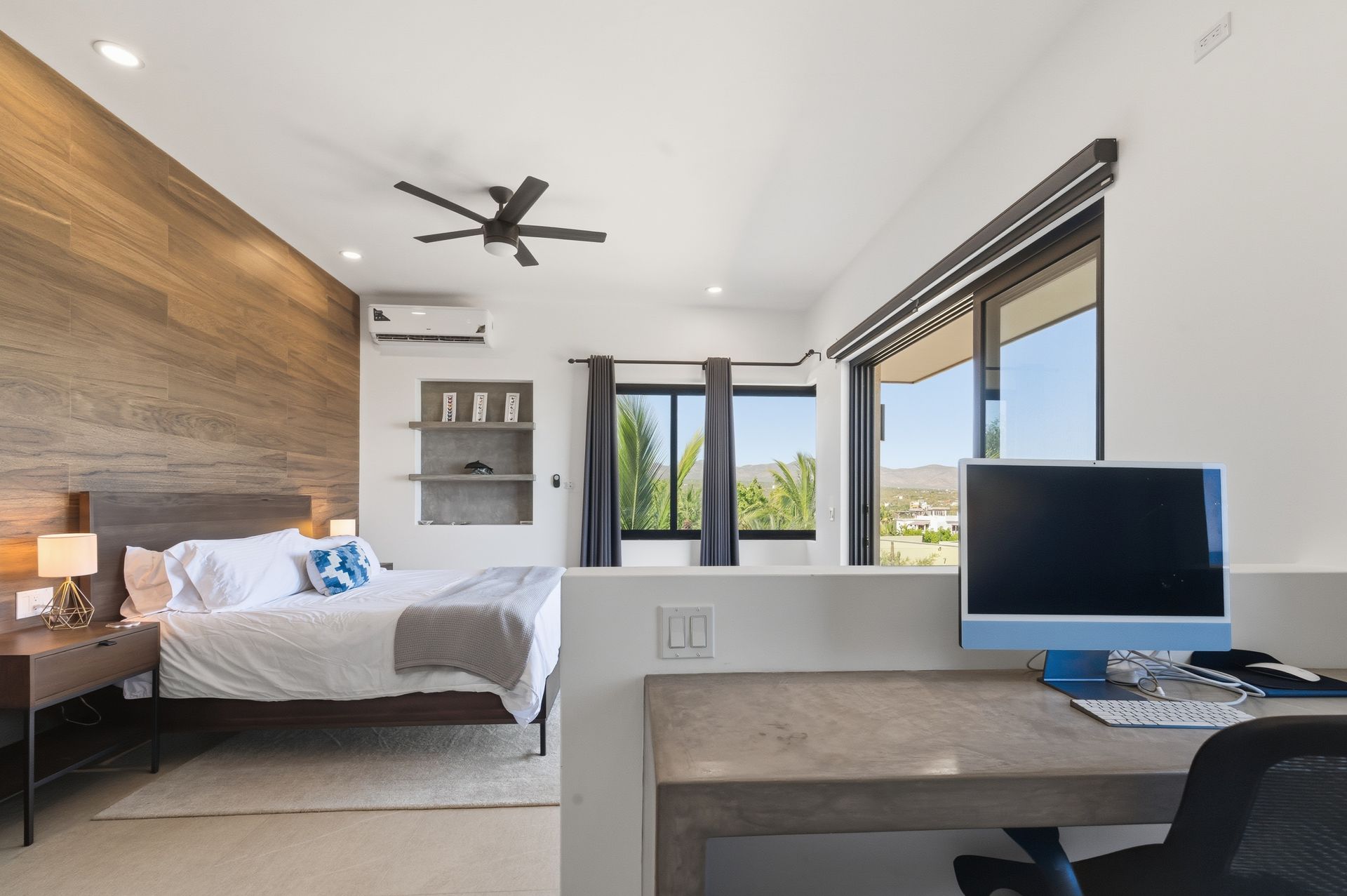 Bedroom with bed, desk, wood accent wall, and windows overlooking a scenic view.