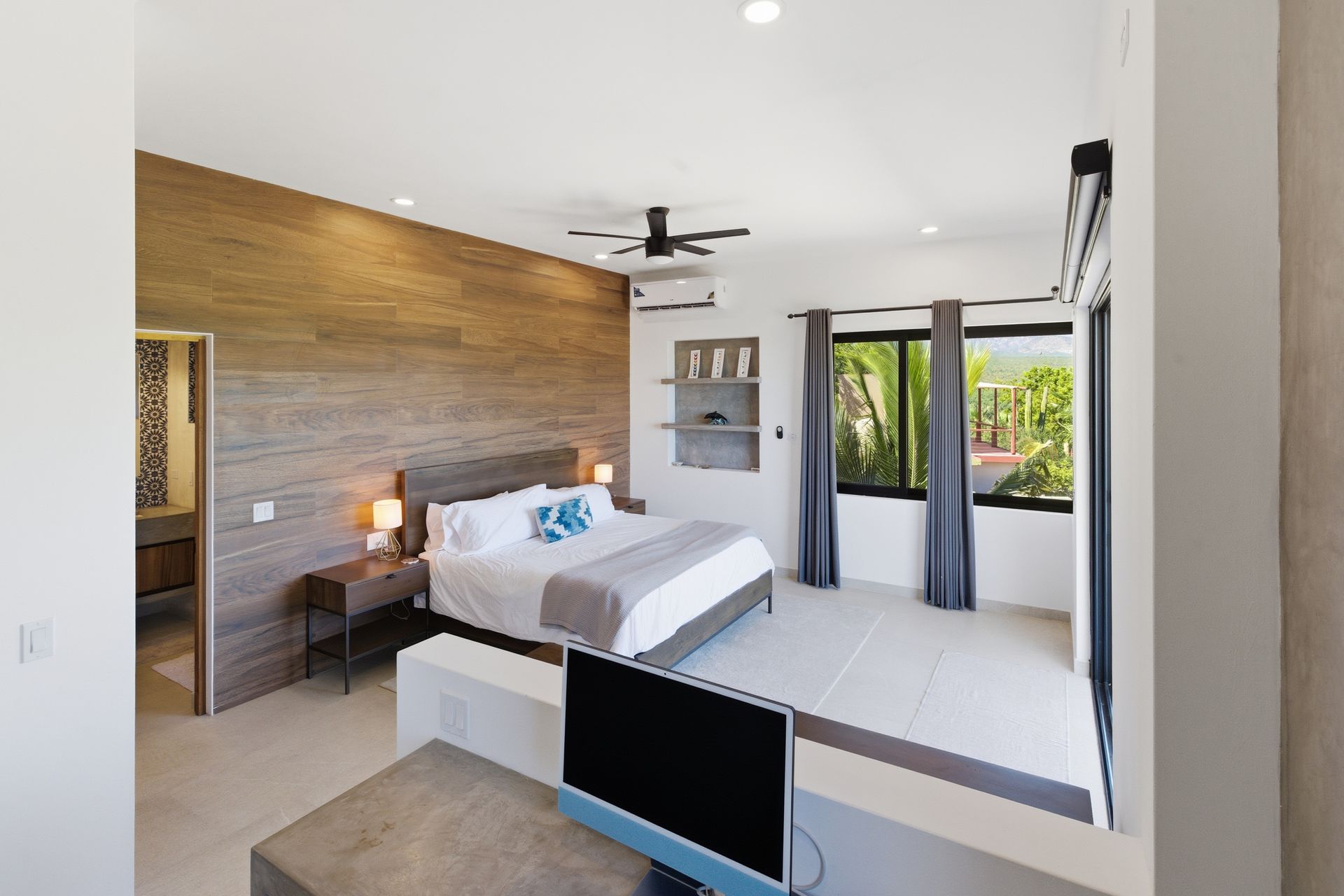 Bedroom with wooden accent wall, bed, nightstand, and window with outdoor view.