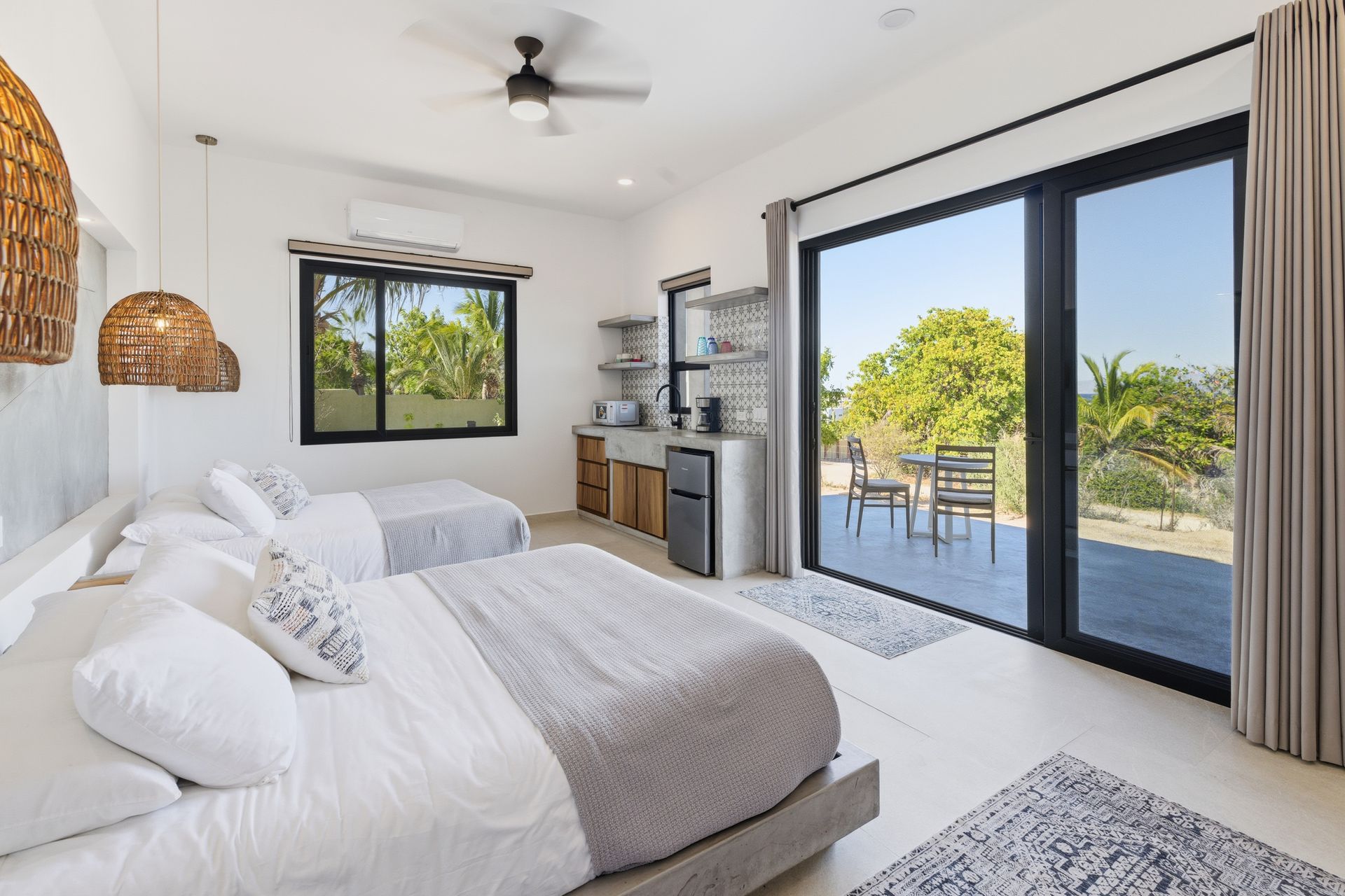 Bedroom with two beds, large windows, and an outdoor patio with a table and chairs.