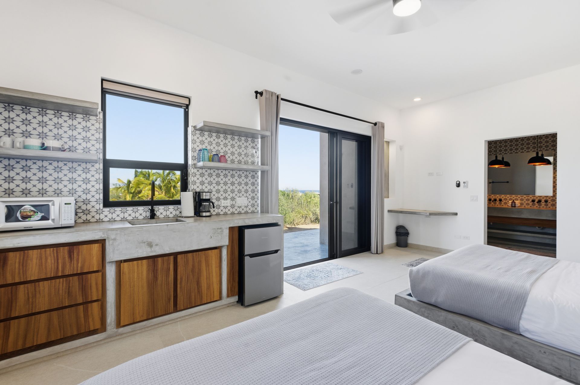 Bright room with two beds, kitchenette, and a sliding glass door to a patio.