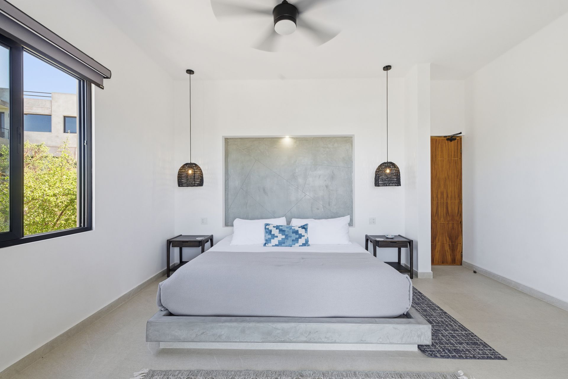 Bedroom with a gray bed, nightstands, and hanging lamps. Features a window, door, and ceiling fan.