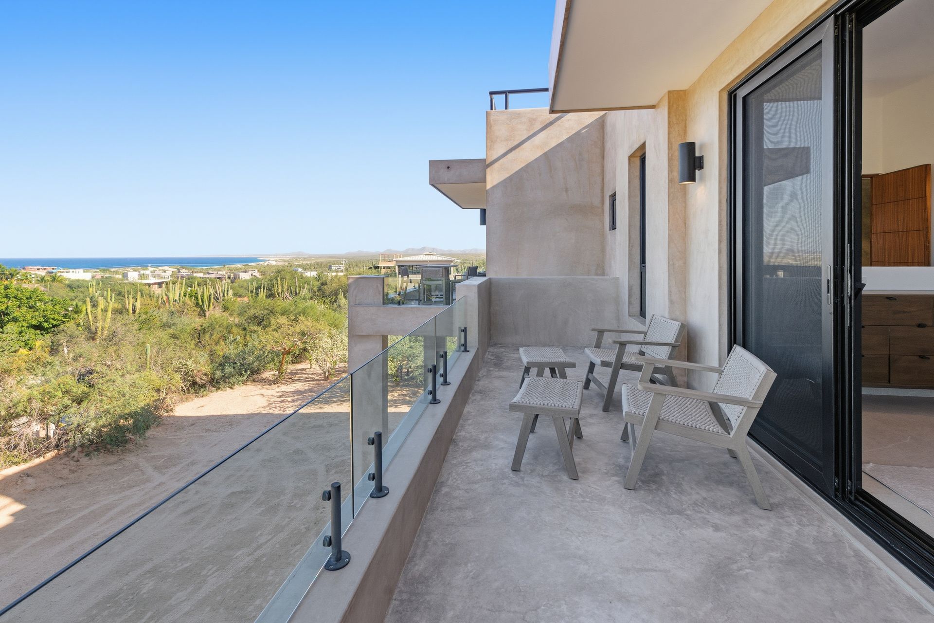 Balcony with chairs overlooking a desert landscape and ocean, under a clear blue sky.