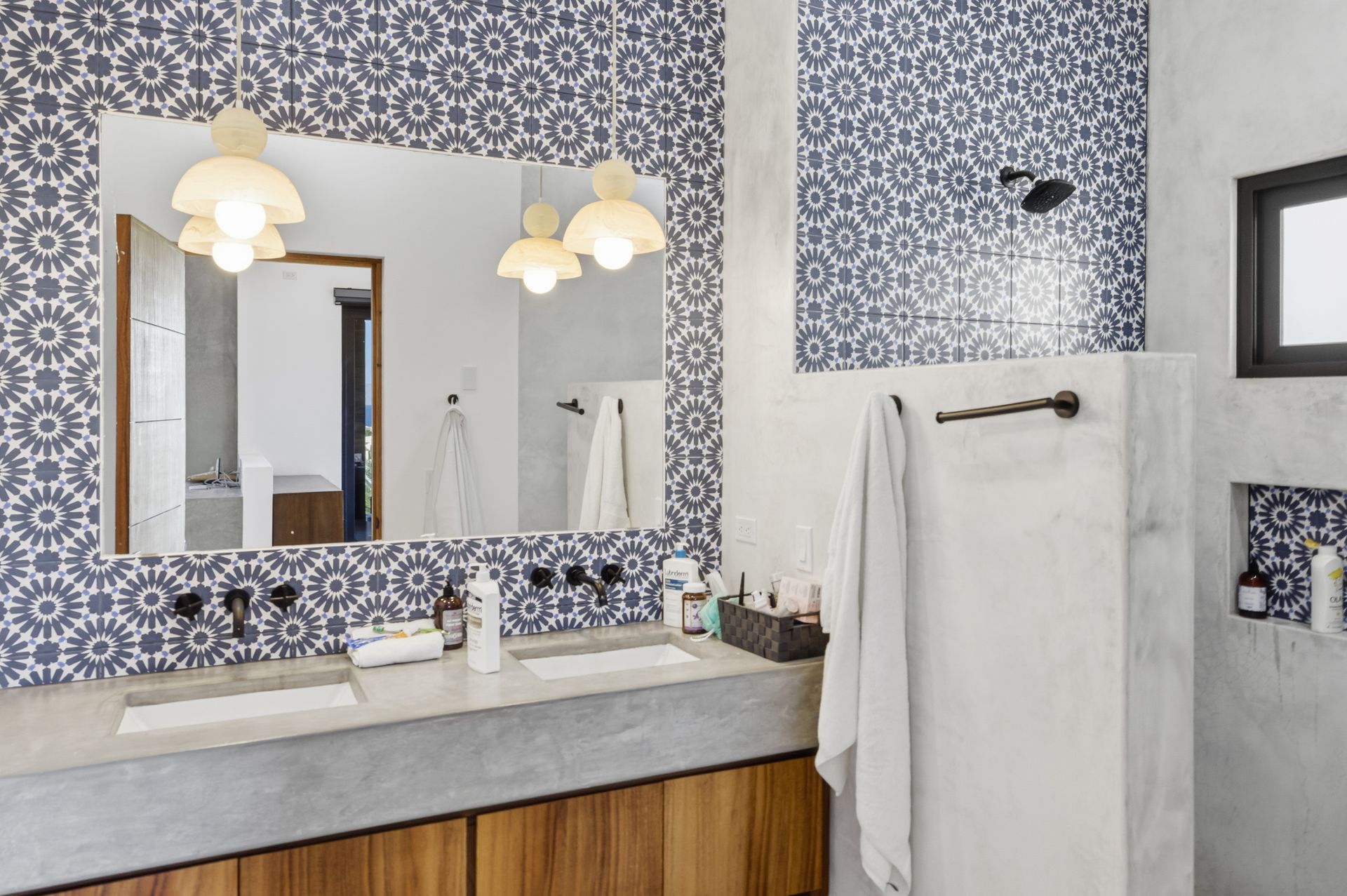 Bathroom with patterned blue tile, concrete countertop, wood cabinets, and pendant lights.