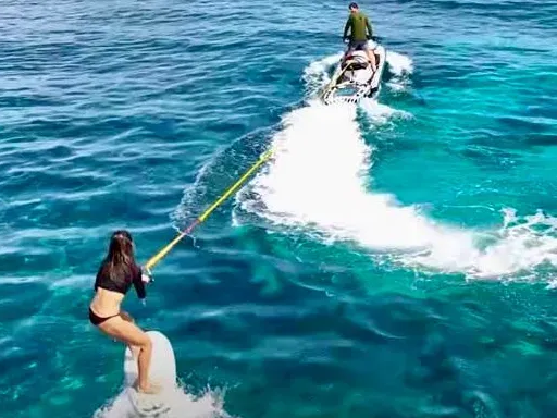 Beach with light sand, blue ocean, rocks, and a mountain range in the background.