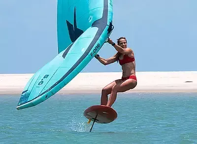 Woman wing foiling on water with blue wing, wearing red bikini.