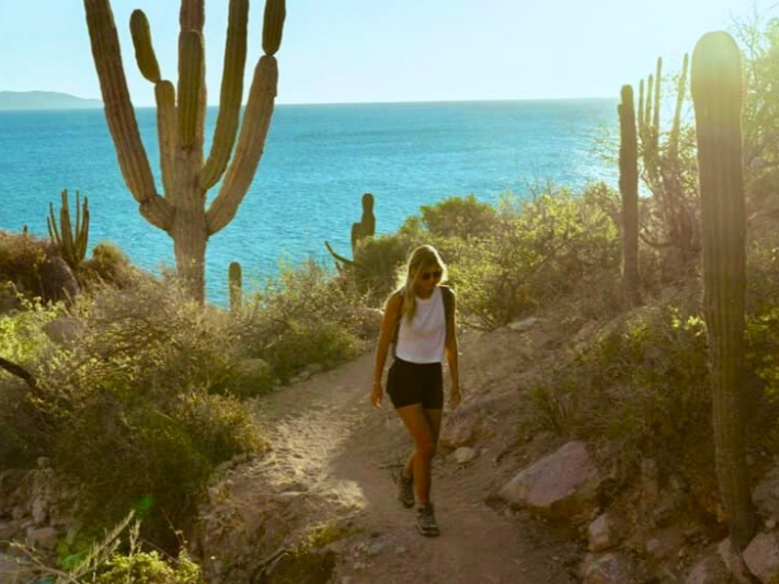 Boy on a small boat holding up a large fish, blue water and coastline in background.