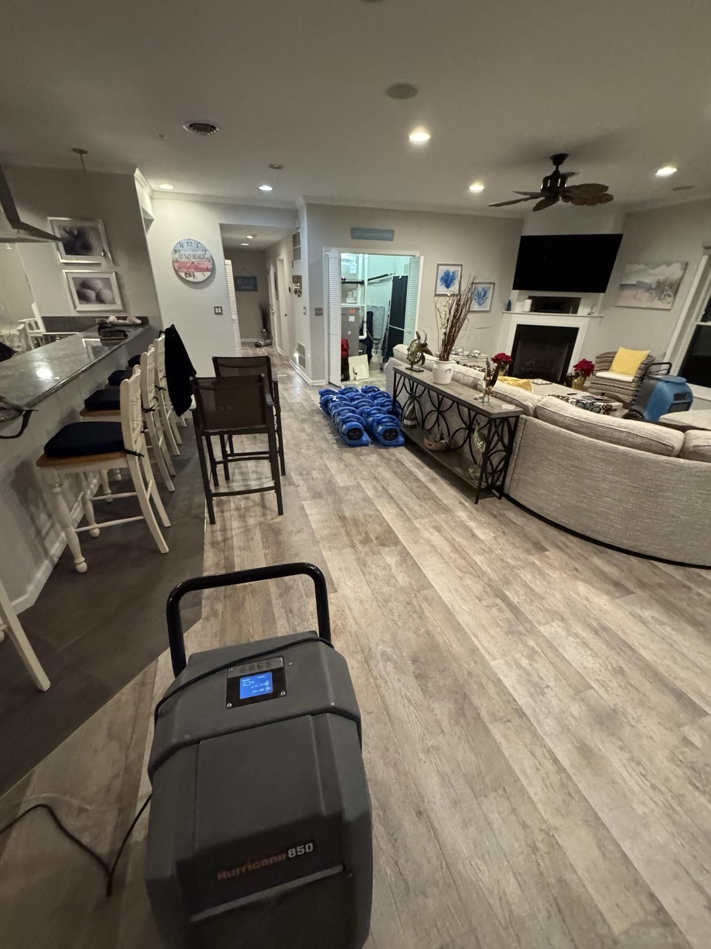 A dehumidifier sits on a living room floor in a home undergoing water damage restoration, with floor fans in the background.