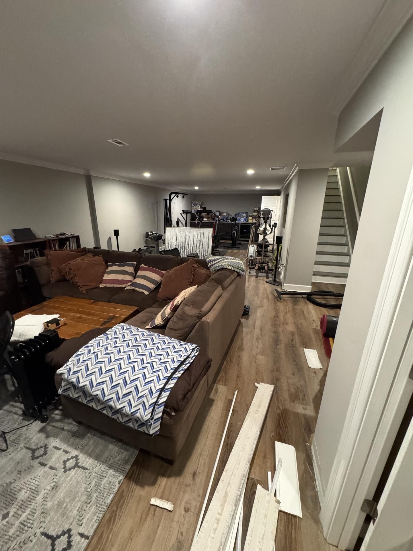 A large brown sectional sofa sits in a living room with wooden floors, with a staircase visible on the right.