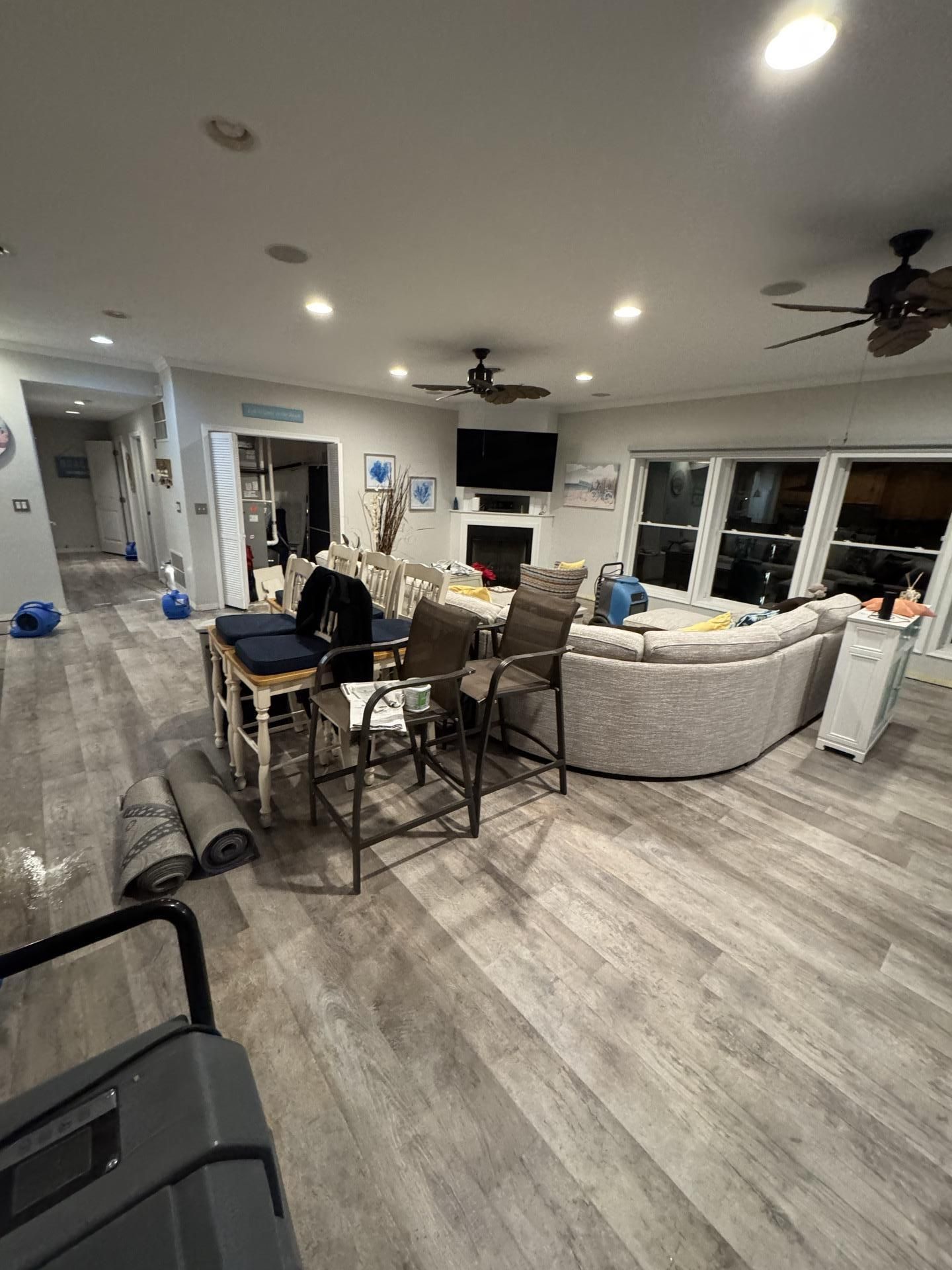 An open-concept living area with light wood floors, a large beige sectional, bar stools, and a fireplace with a TV.