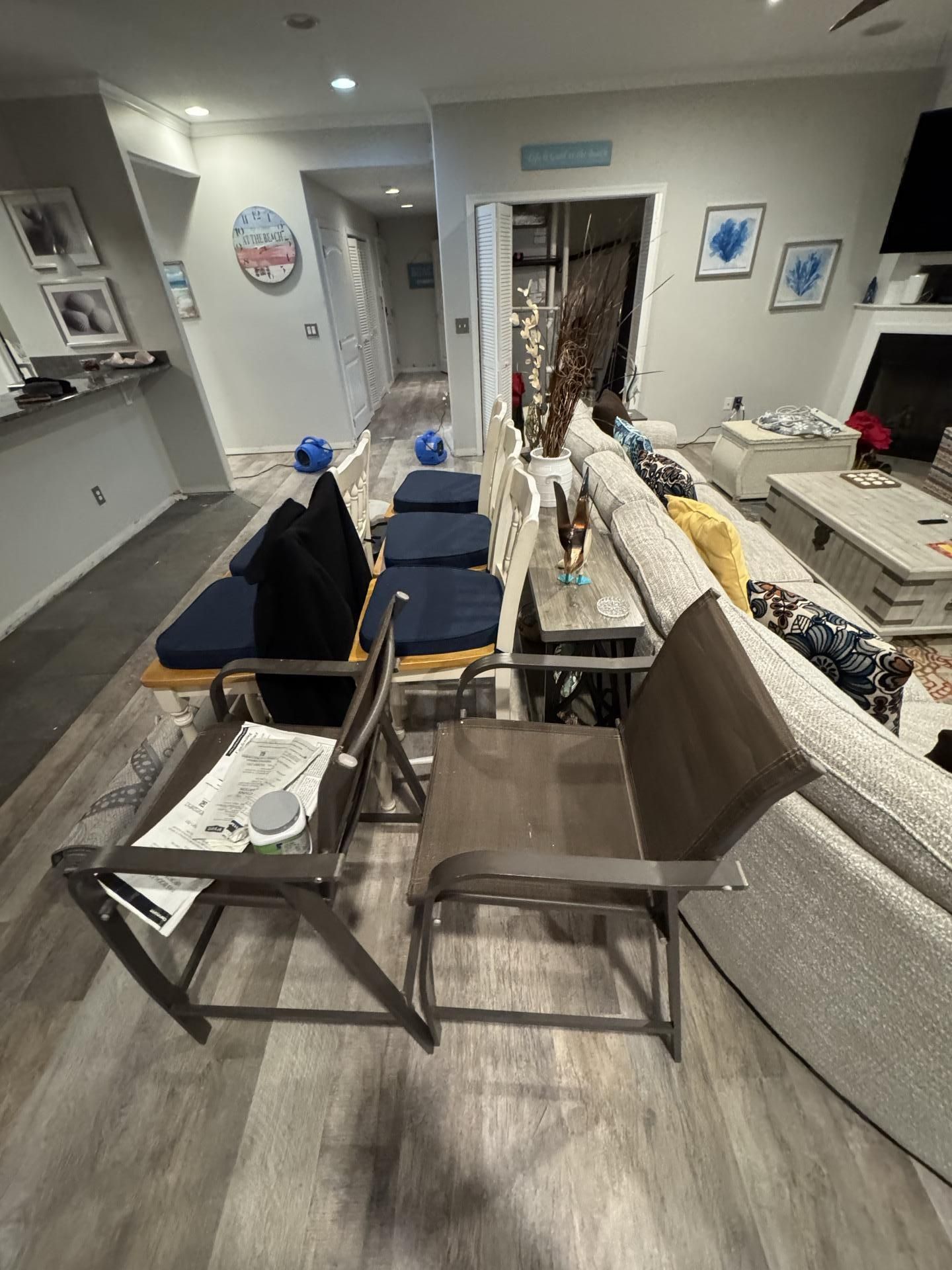 Two brown outdoor chairs sit in a living room, positioned in front of a sofa and a row of cushion-topped dining chairs.