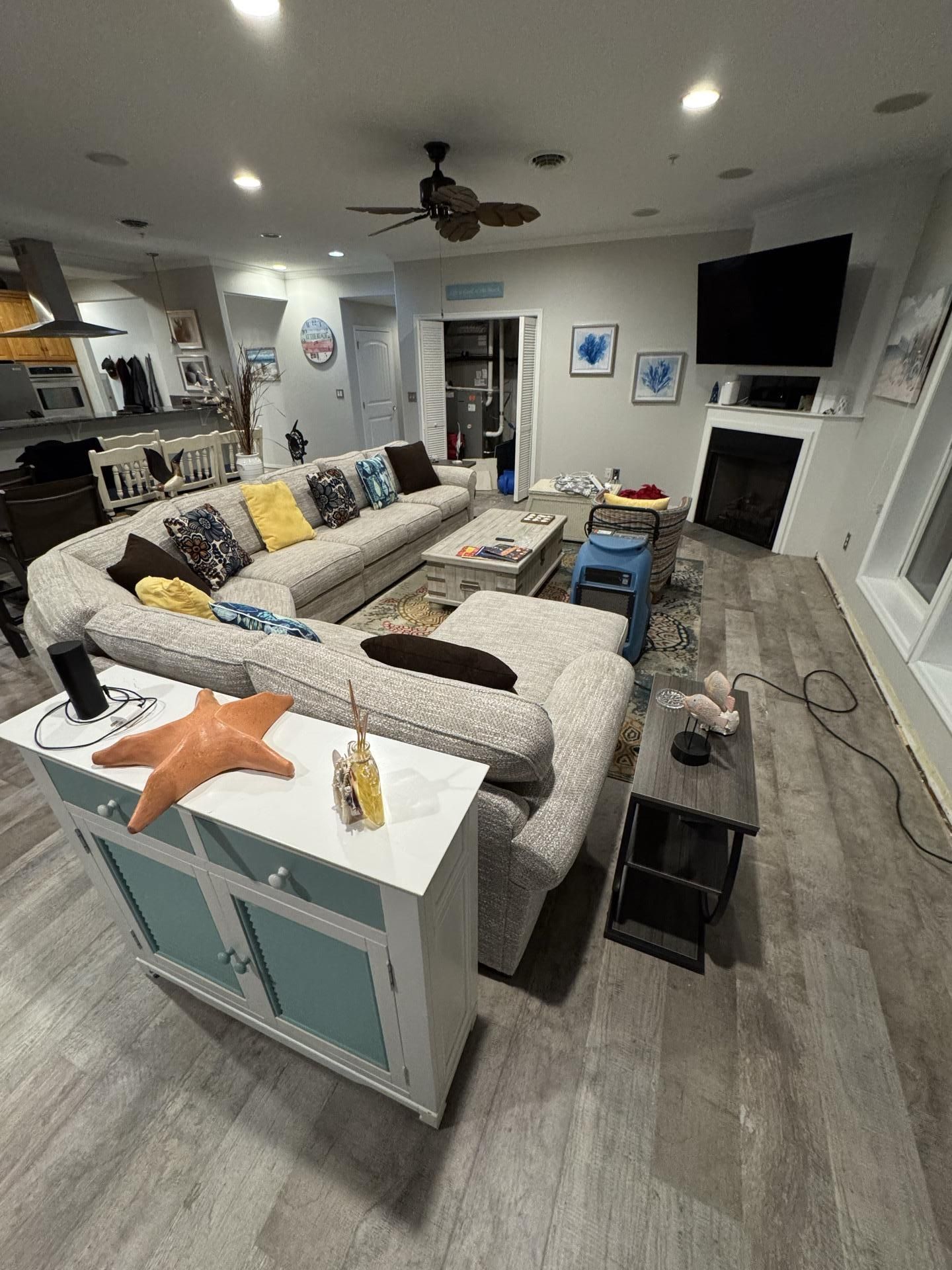 A spacious, open-concept living room with a large gray sectional sofa, light wood floors, a fireplace, and a TV.