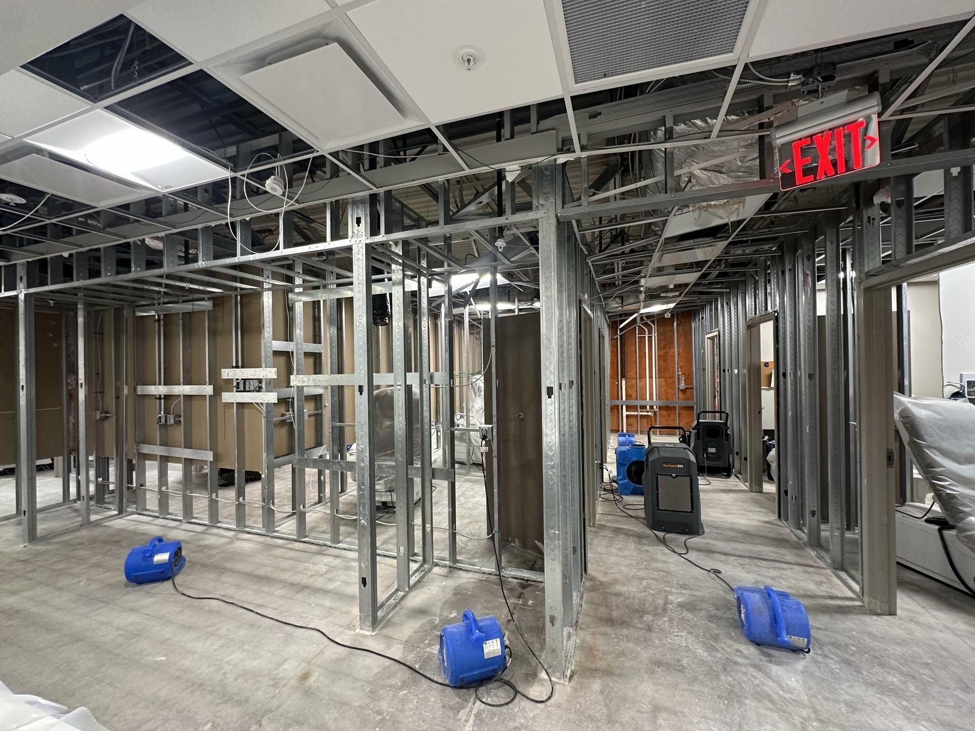Metal framing in a construction site with industrial floor fans used for drying, showing exposed walls and ceiling.