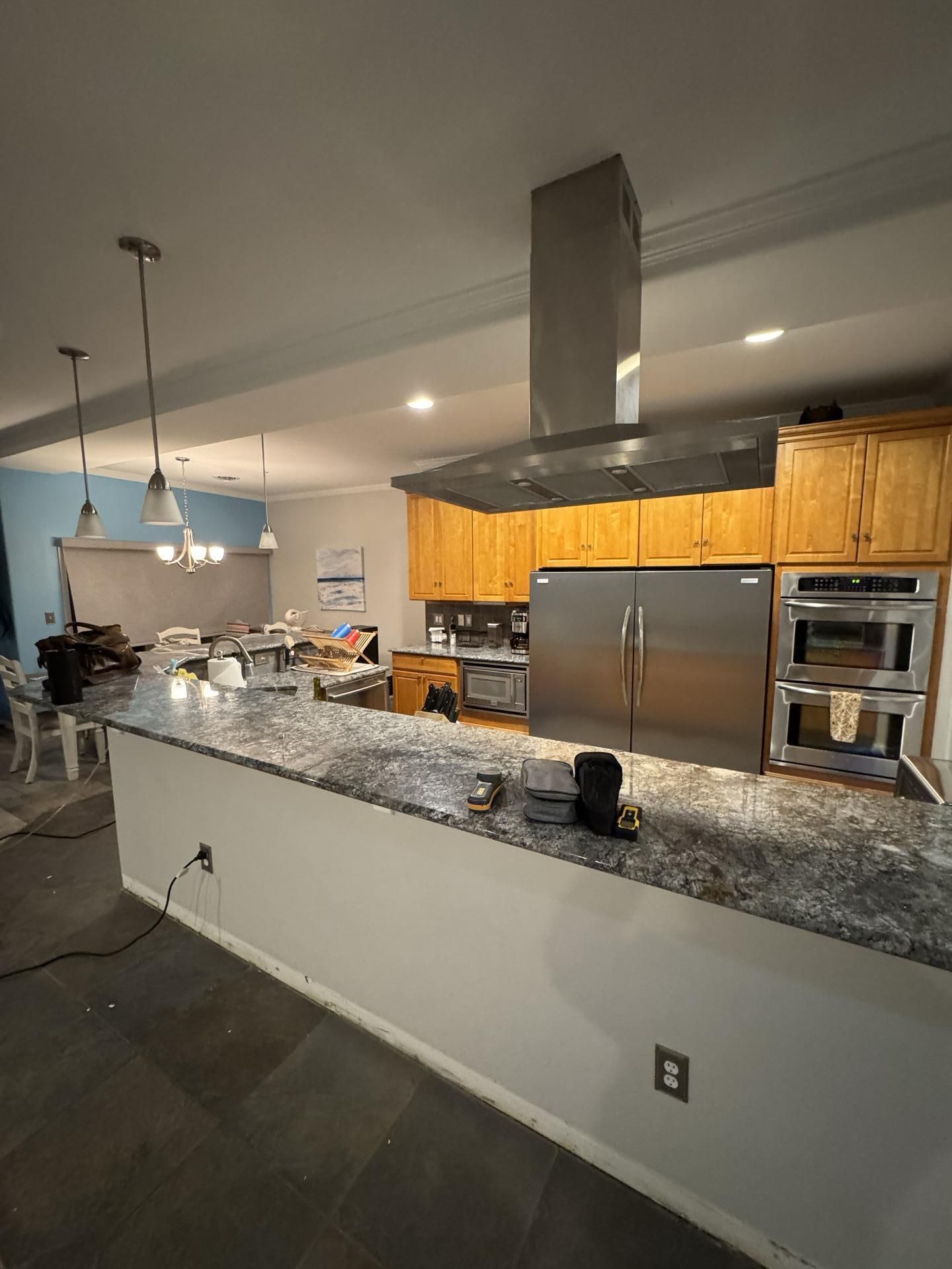 Kitchen featuring a granite breakfast bar, stainless steel refrigerator, double ovens, and a large overhead range hood.