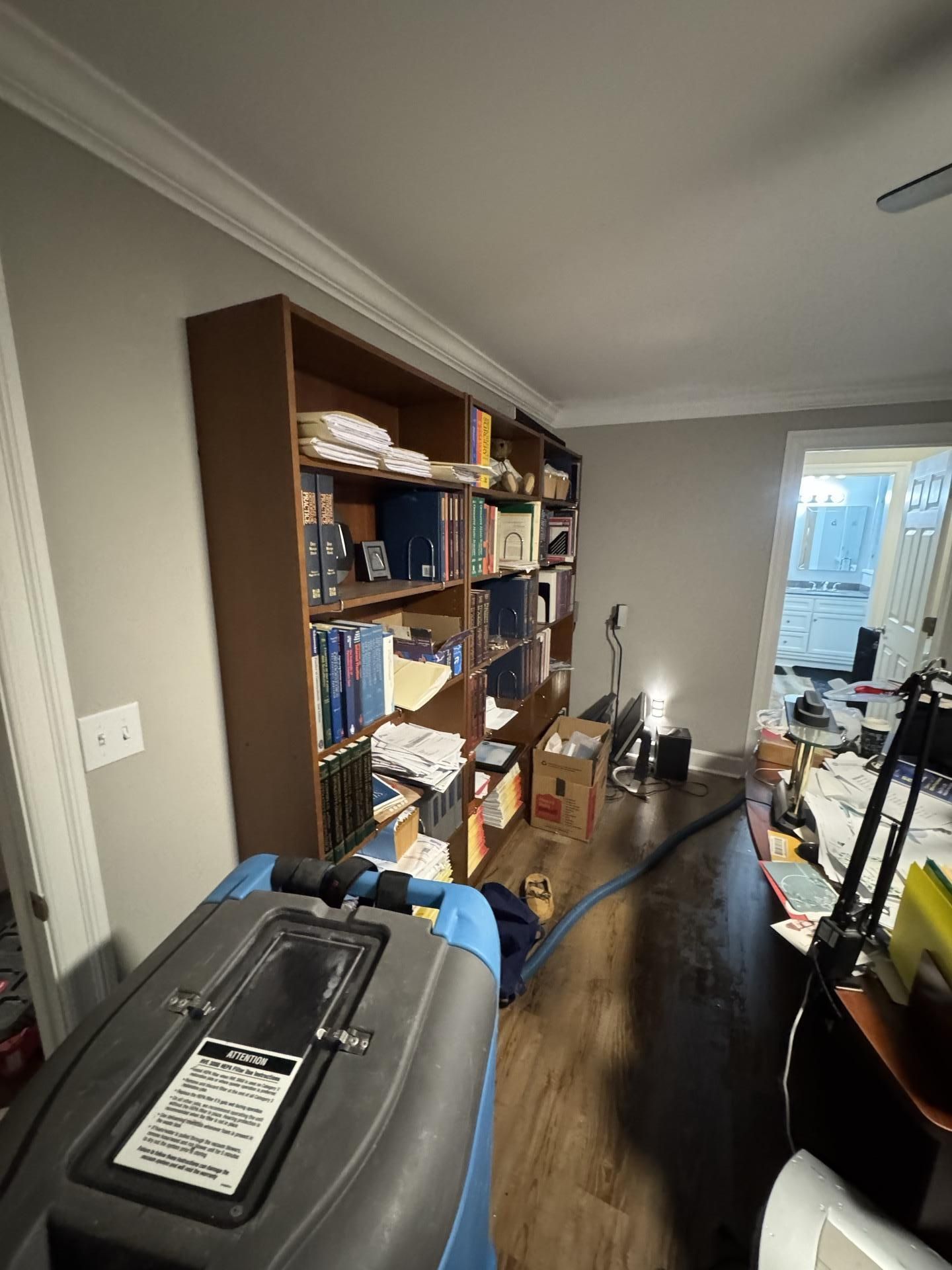 A room with a large wooden bookcase, a piece of industrial cleaning equipment in the foreground, and a view of a doorway.