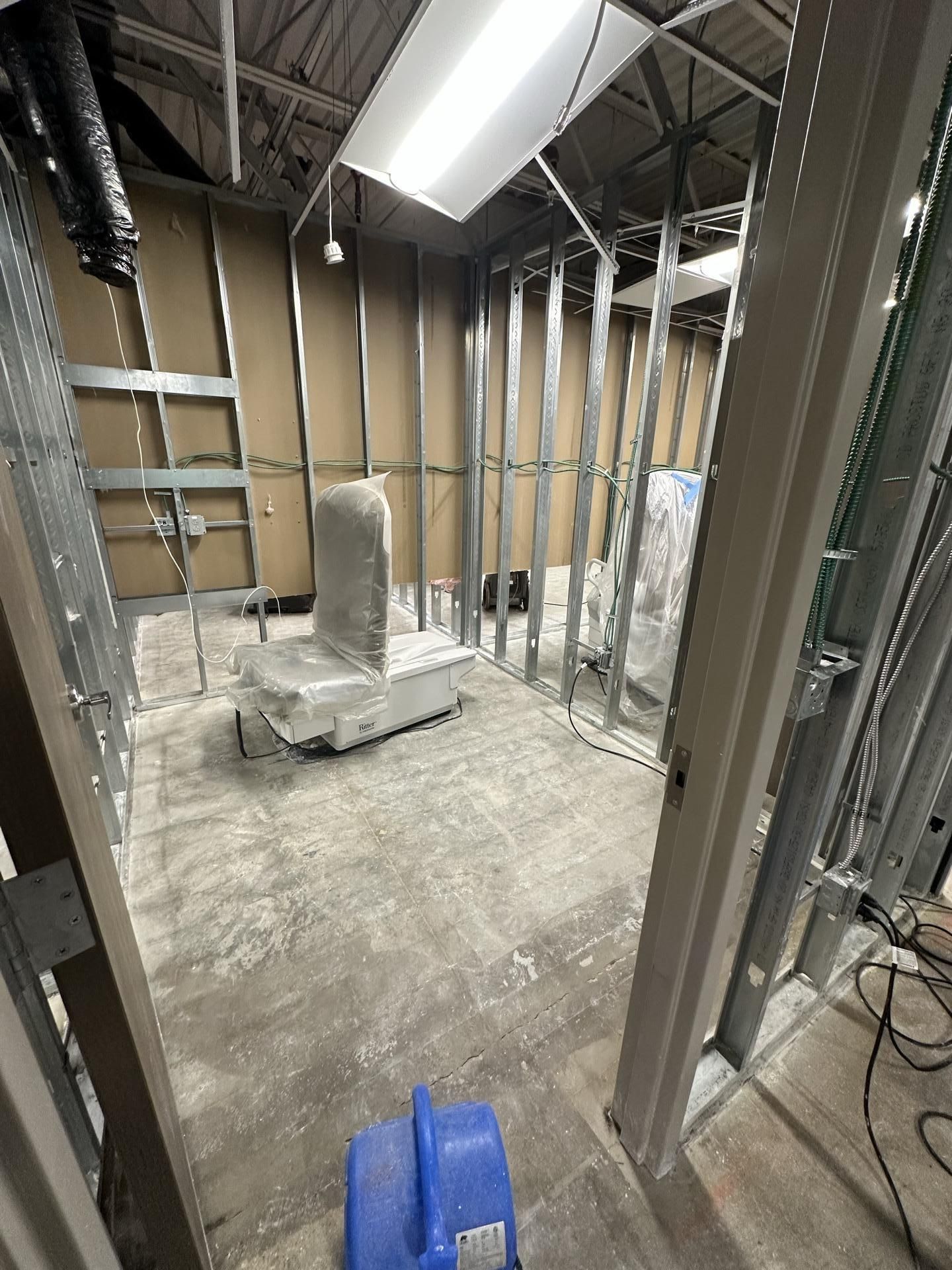 Construction site view of an unfinished room with metal wall studs, concrete floors, and furniture covered in plastic.