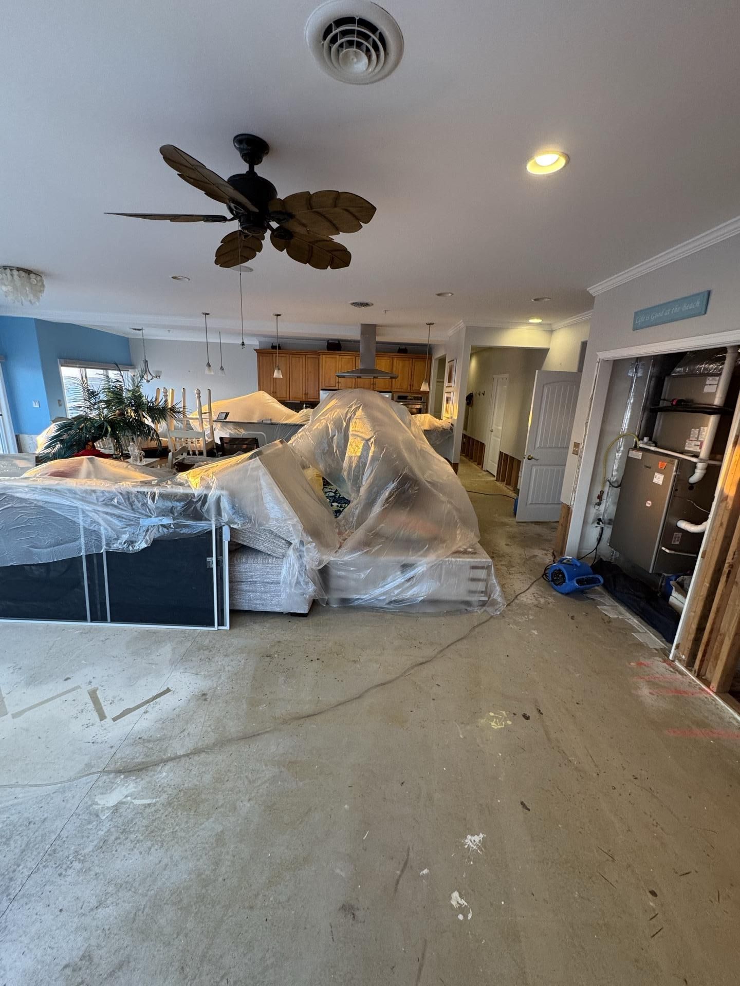 A room under renovation with covered furniture, a ceiling fan, and an exposed utility closet with a furnace.