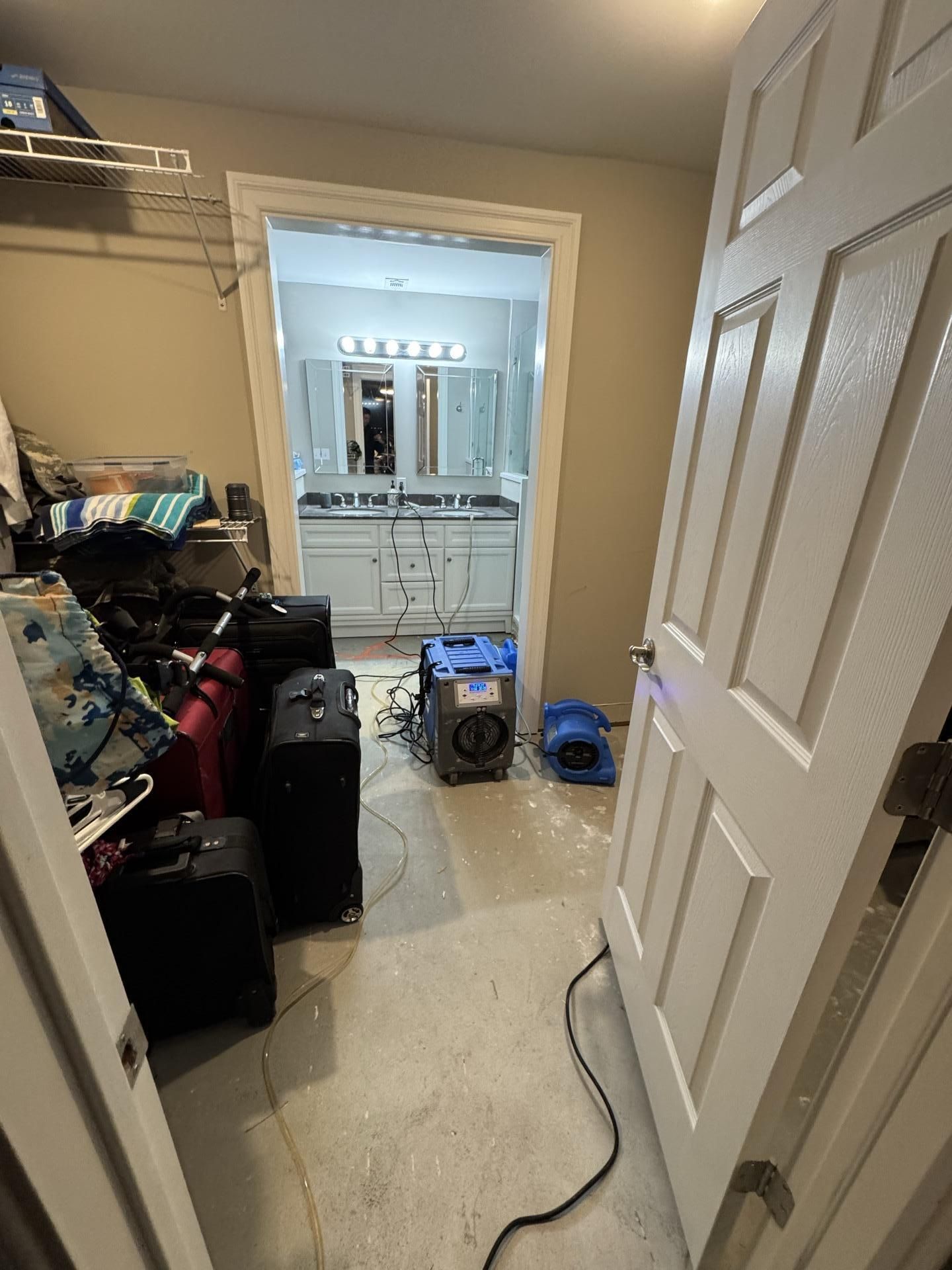 A view through a doorway into a room with luggage and specialized drying equipment running on a bare floor.