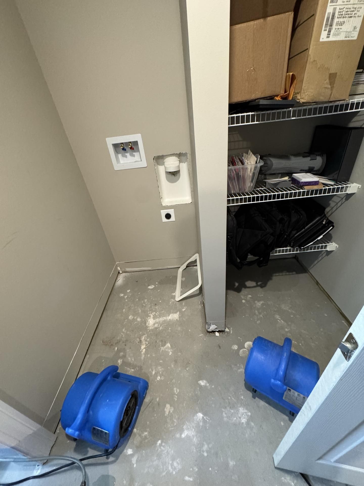 Two blue industrial air movers sitting on a concrete floor in a laundry area undergoing water damage remediation.