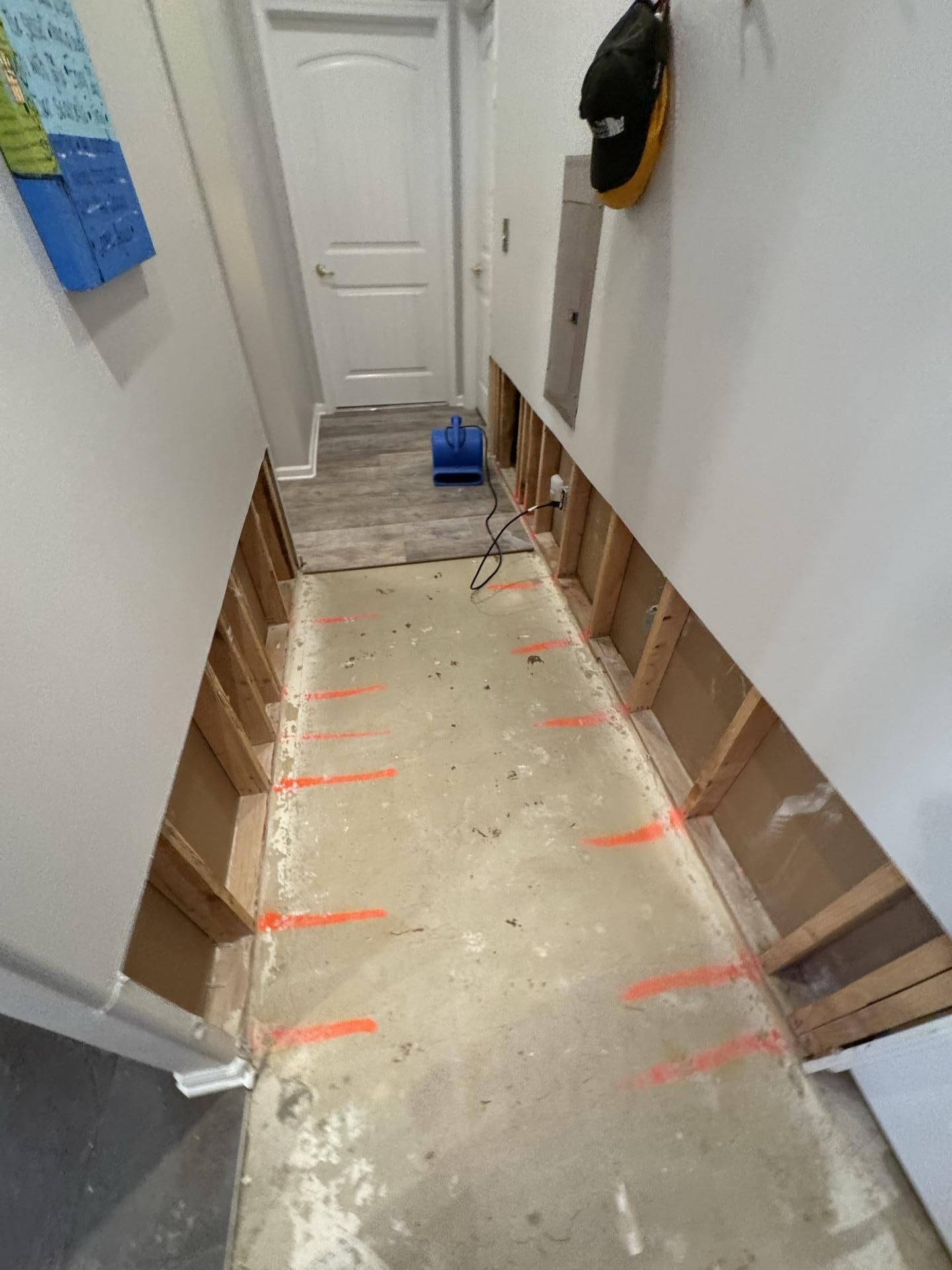 A residential hallway under renovation, with drywall removed from the lower walls and orange marks on the concrete floor.