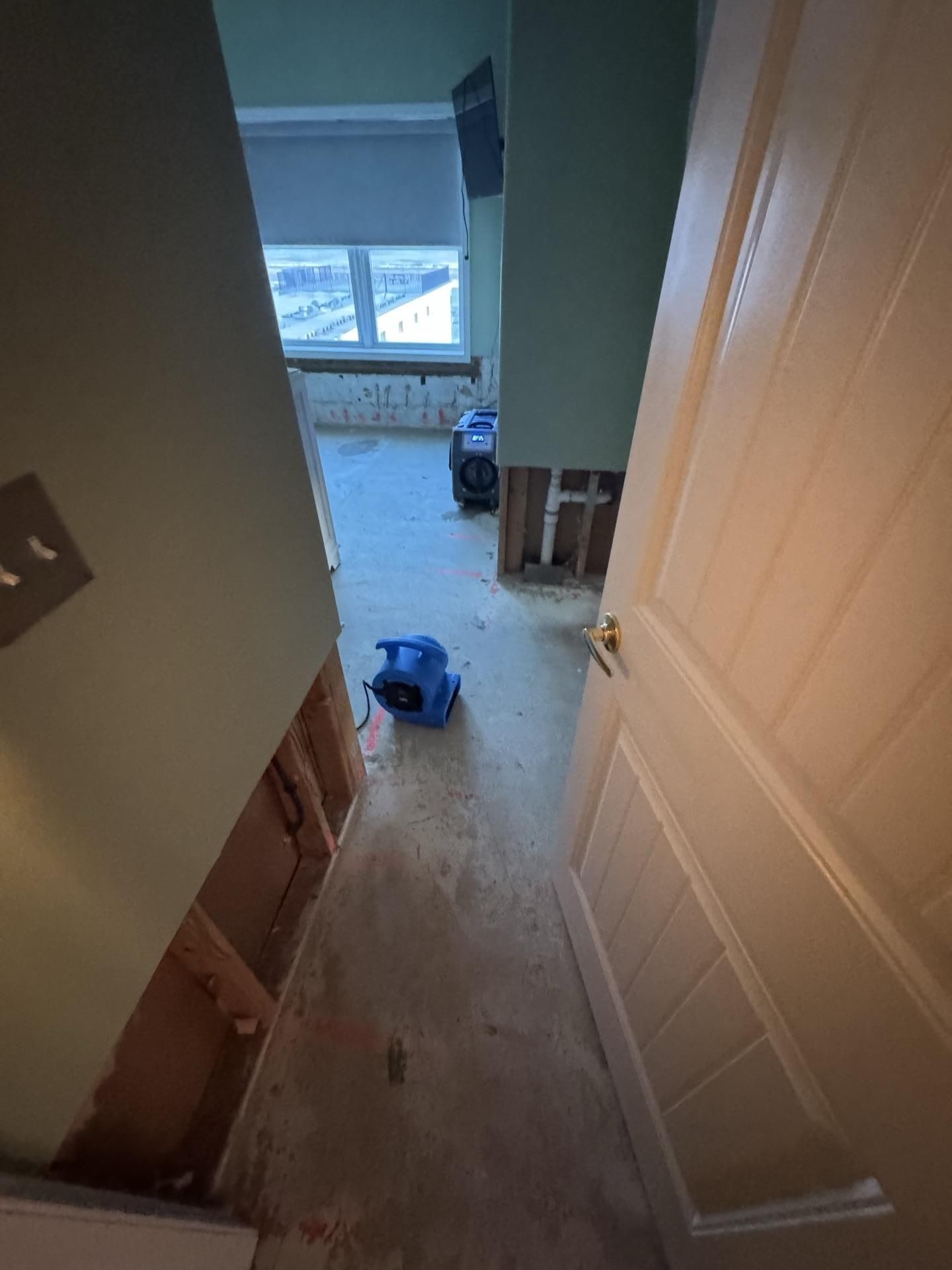 A room undergoing water damage restoration with opened wall sections and blue air movers on the floor.