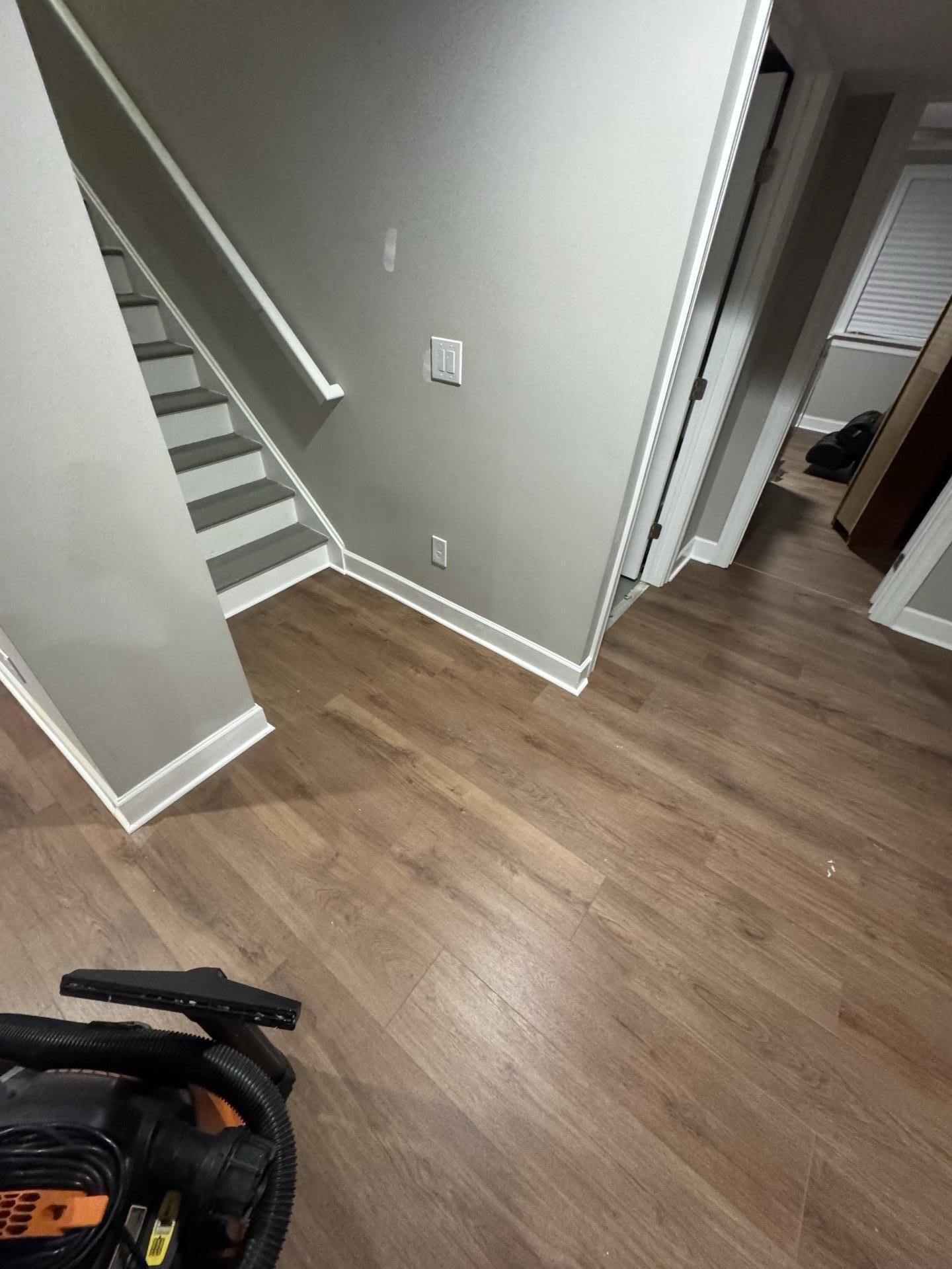 An indoor hallway with light grey walls, brown wood flooring, and a staircase leading to an upper level.