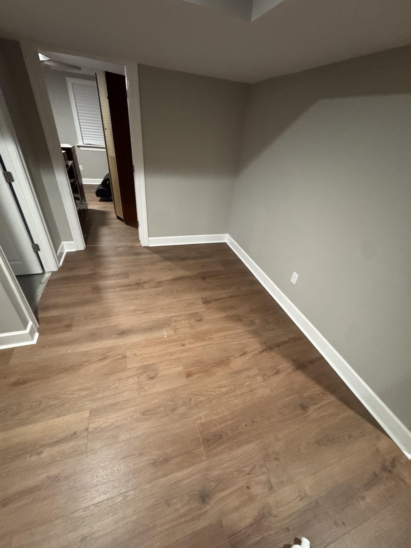 An empty room with gray walls, white baseboards, and light-brown wood-look flooring, viewed from a doorway.
