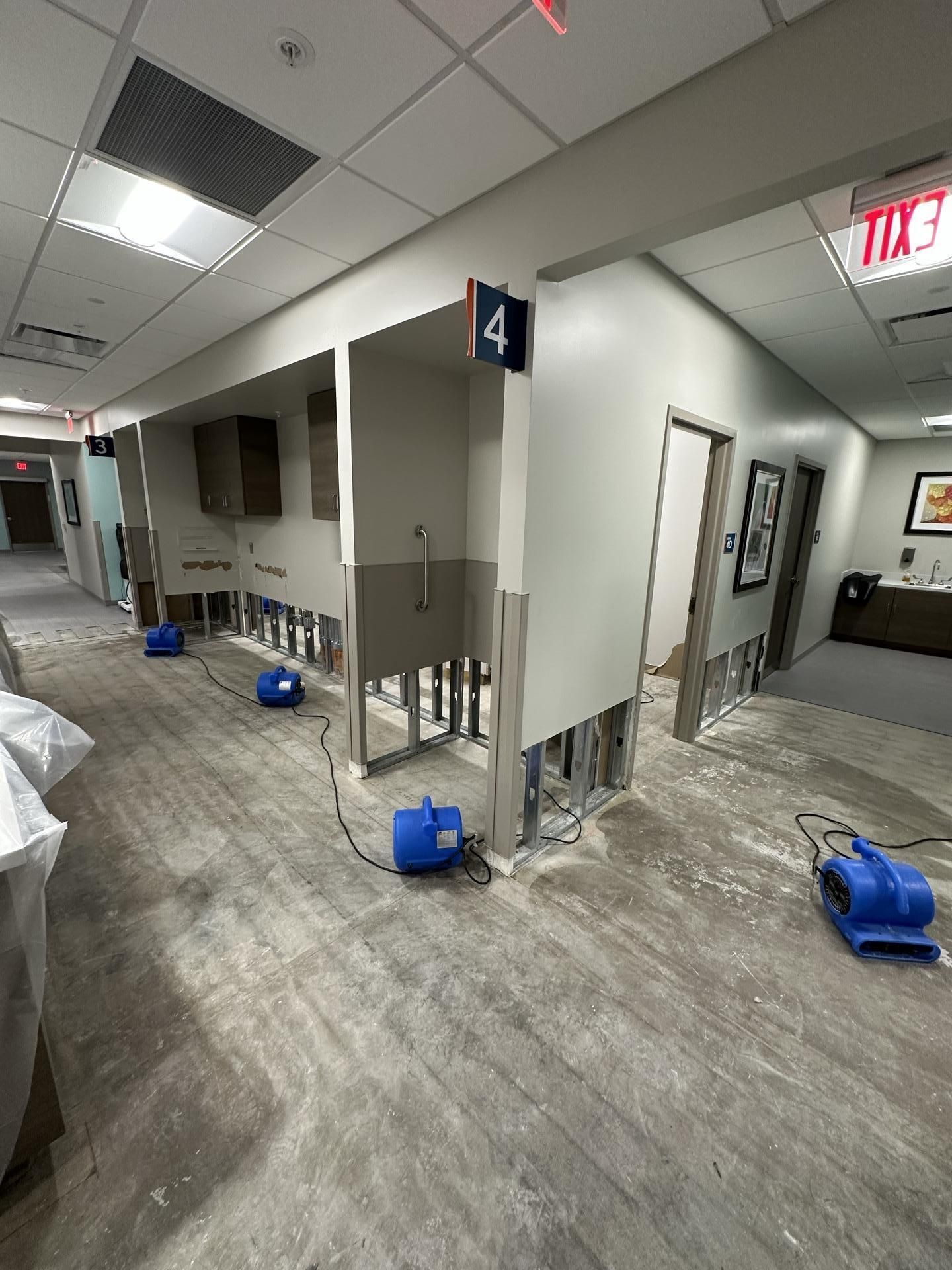 A hallway in a building undergoing water damage repair with blue industrial fans drying the stripped, exposed wall studs.
