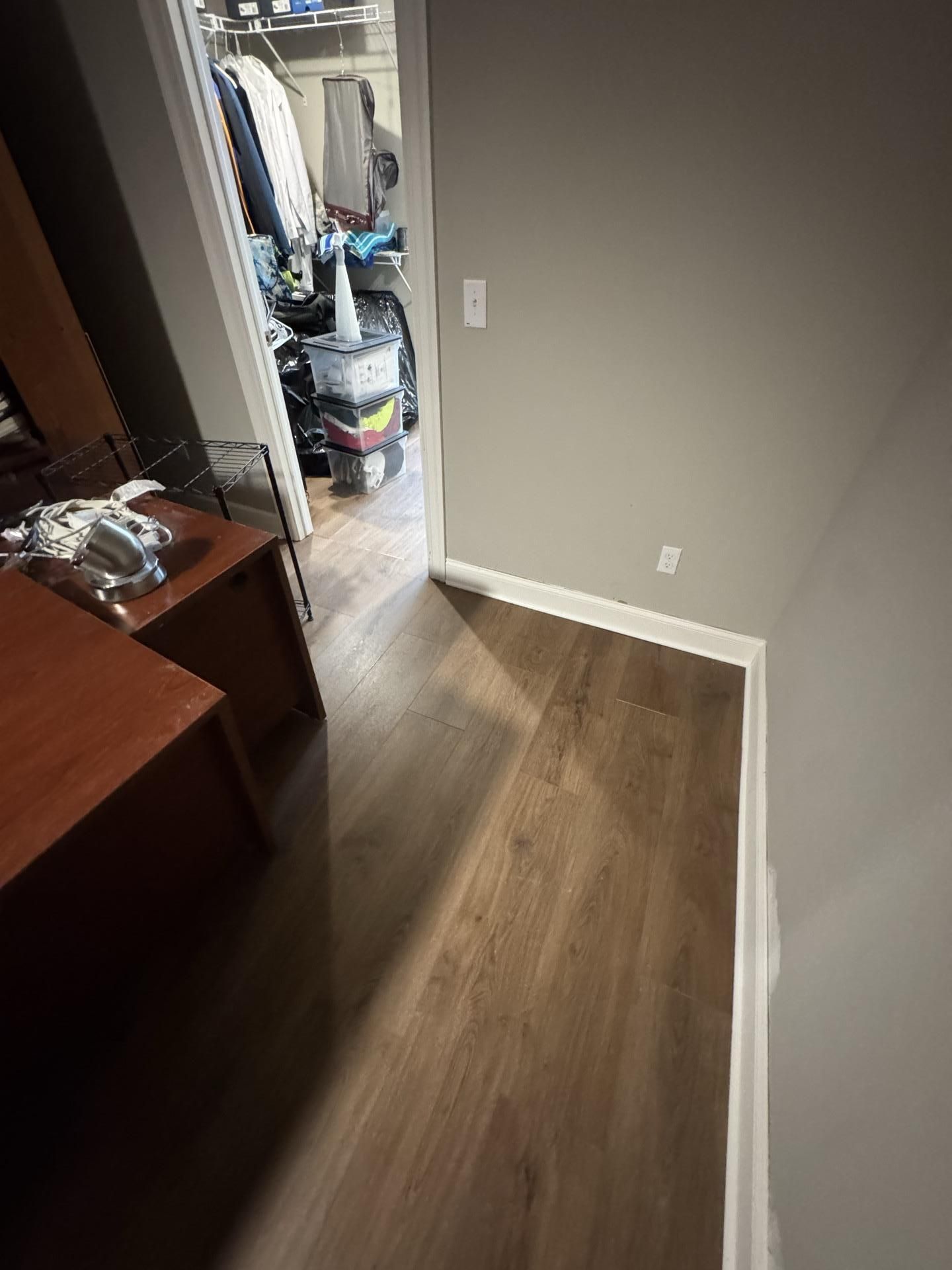 A view of wood-look flooring leading to a doorway, with a brown desk on the left and a gray wall on the right.