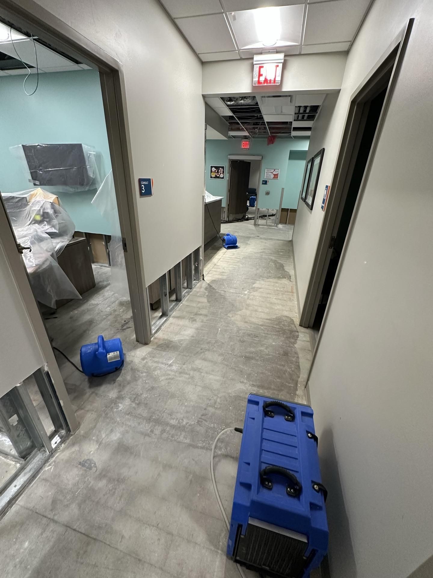 A commercial hallway undergoing water damage restoration with industrial dehumidifiers on the floor and open wall studs.