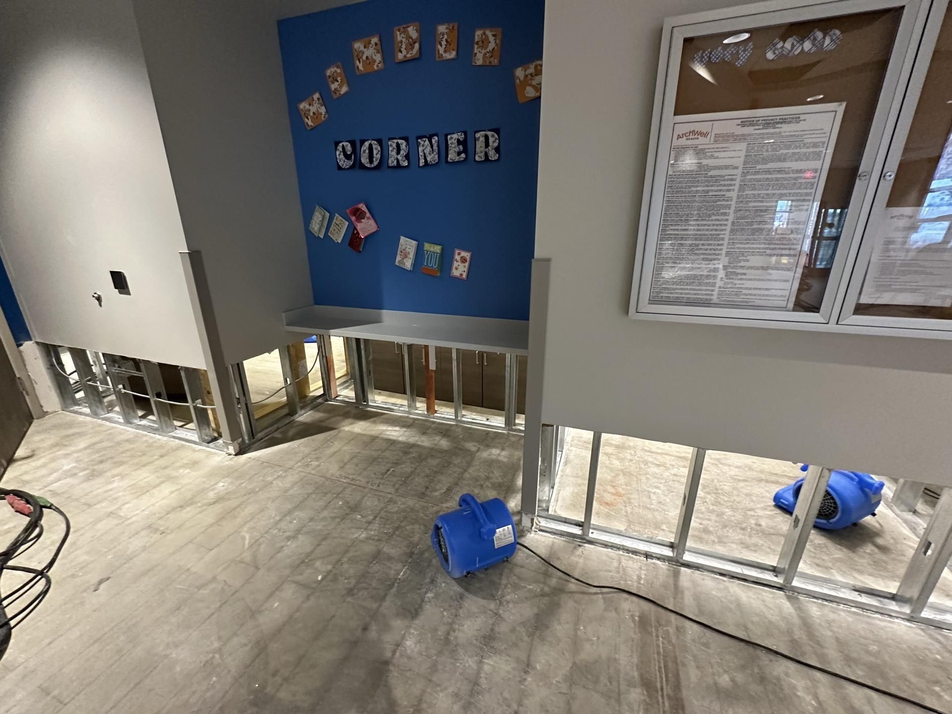 An indoor space undergoing water damage remediation, with lower wall sections removed, metal studs exposed, and air movers.