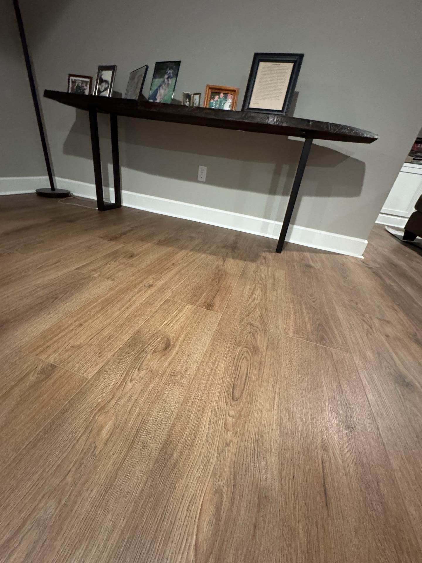 A long, dark live-edge wood console table stands against a gray wall above wood-look flooring, displaying framed photos.