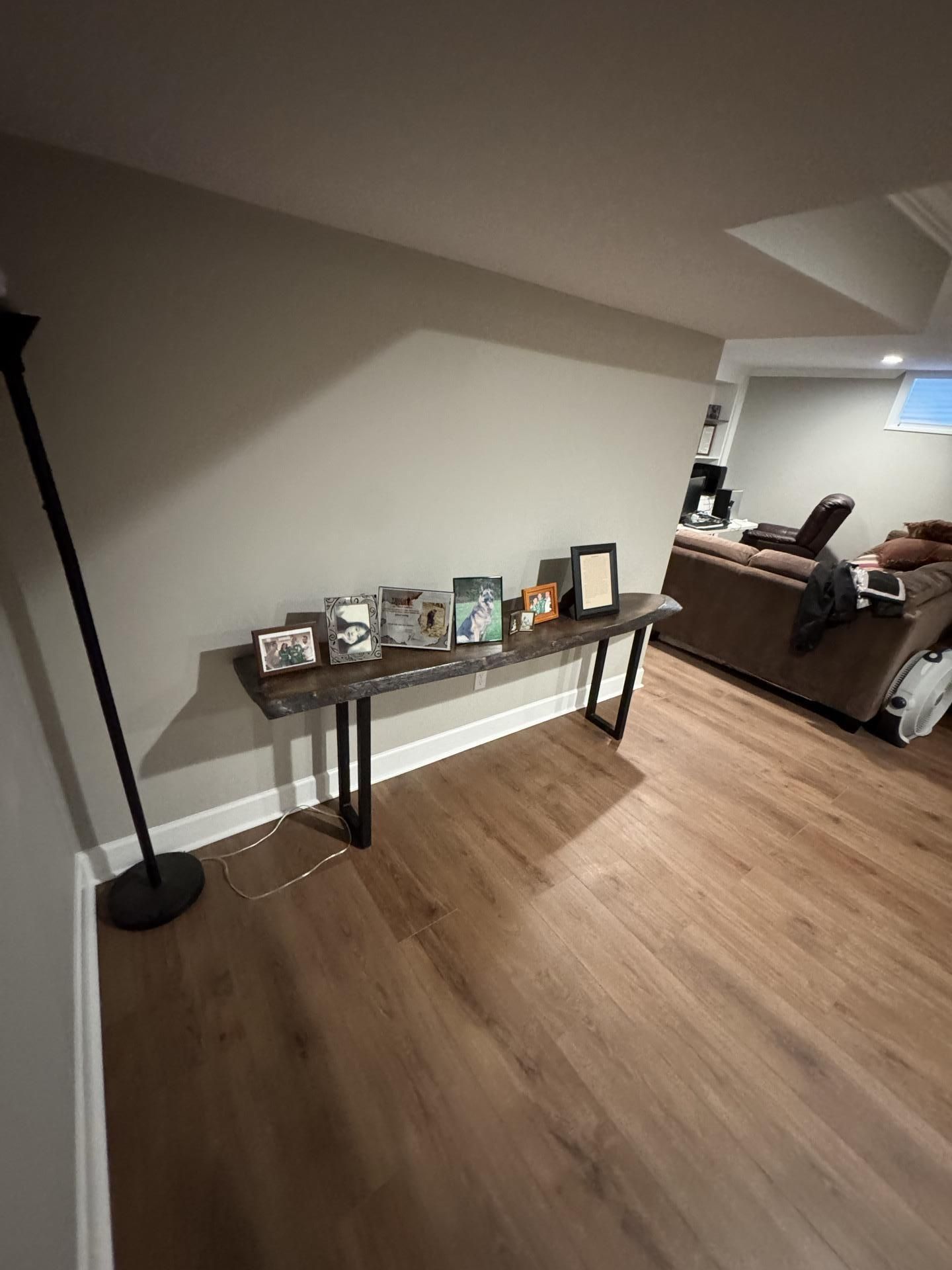 A long, dark wood console table with metal legs stands against a gray wall, displaying small picture frames.
