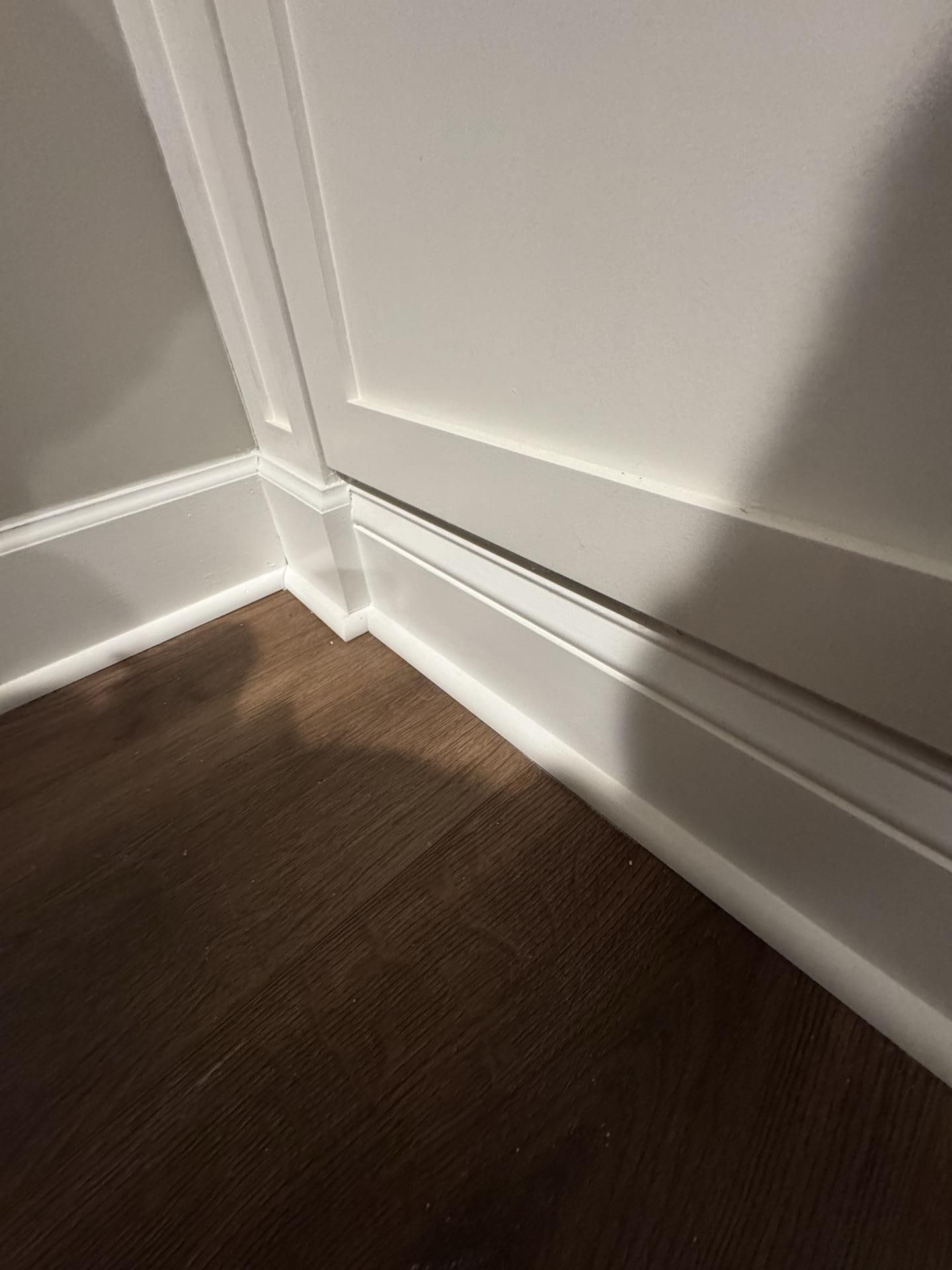 A corner where white wall molding meets a dark wood floor, showing a small gap between the trim and the wall.