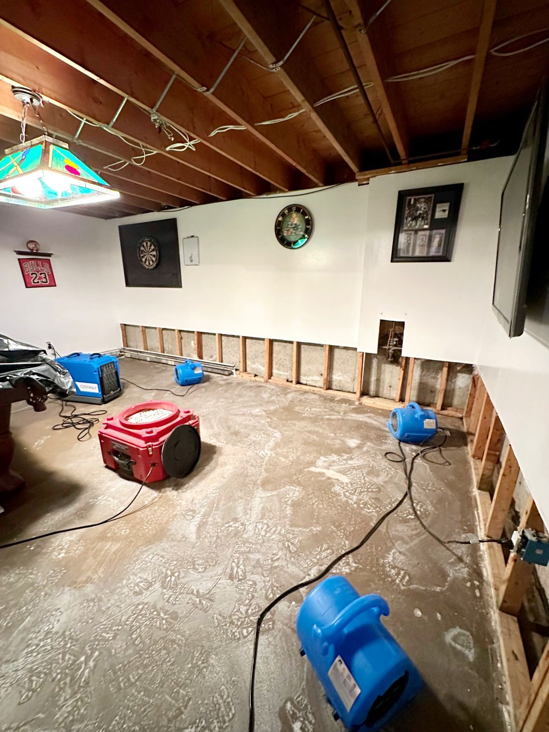 Basement renovation or water damage restoration with drying fans placed on a concrete floor in front of exposed wall studs.