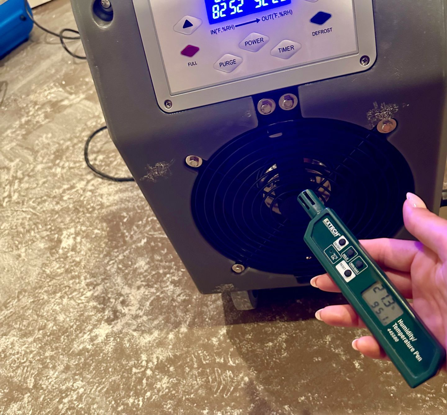 A person holds a digital humidity and temperature pen to test the air output of a portable industrial dehumidifier.