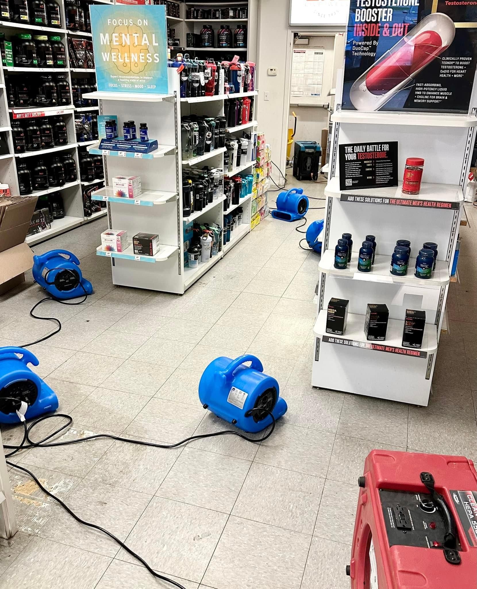 Several blue industrial floor dryers are positioned throughout a retail store aisle during a flood cleanup effort.