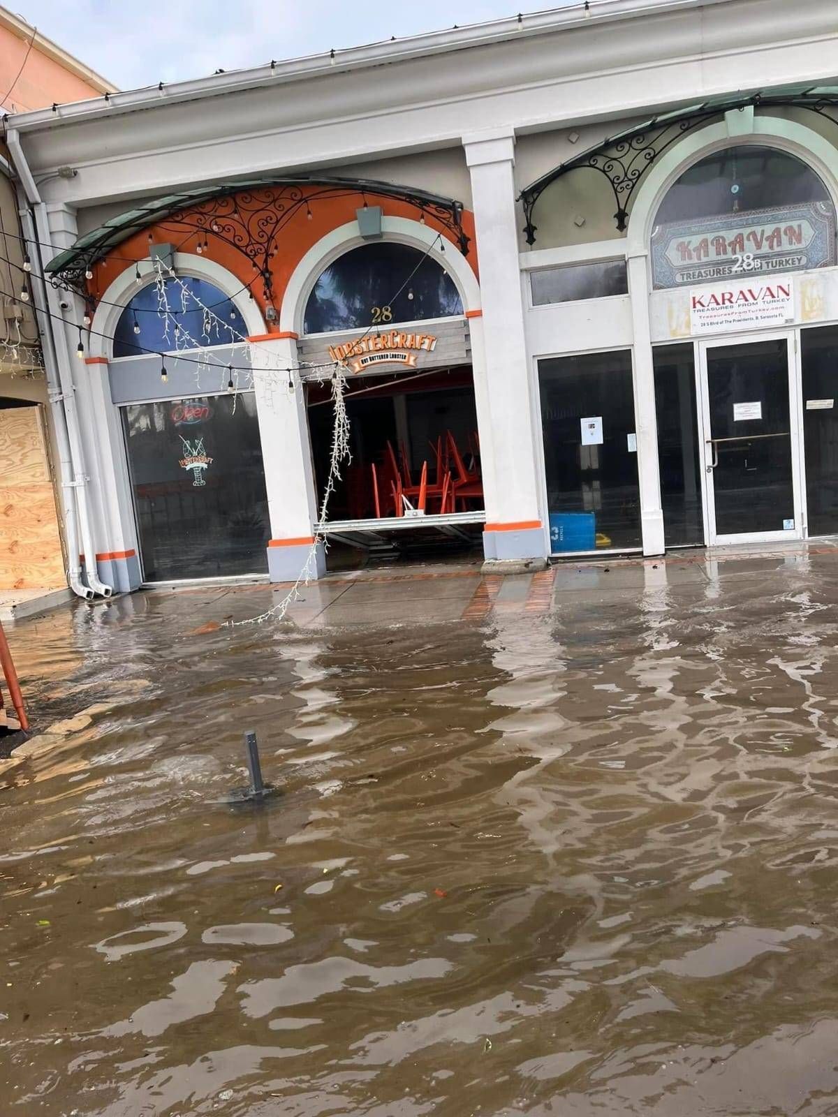 Flooded street in front of a row of storefronts, with dark water reaching the base of the buildings.