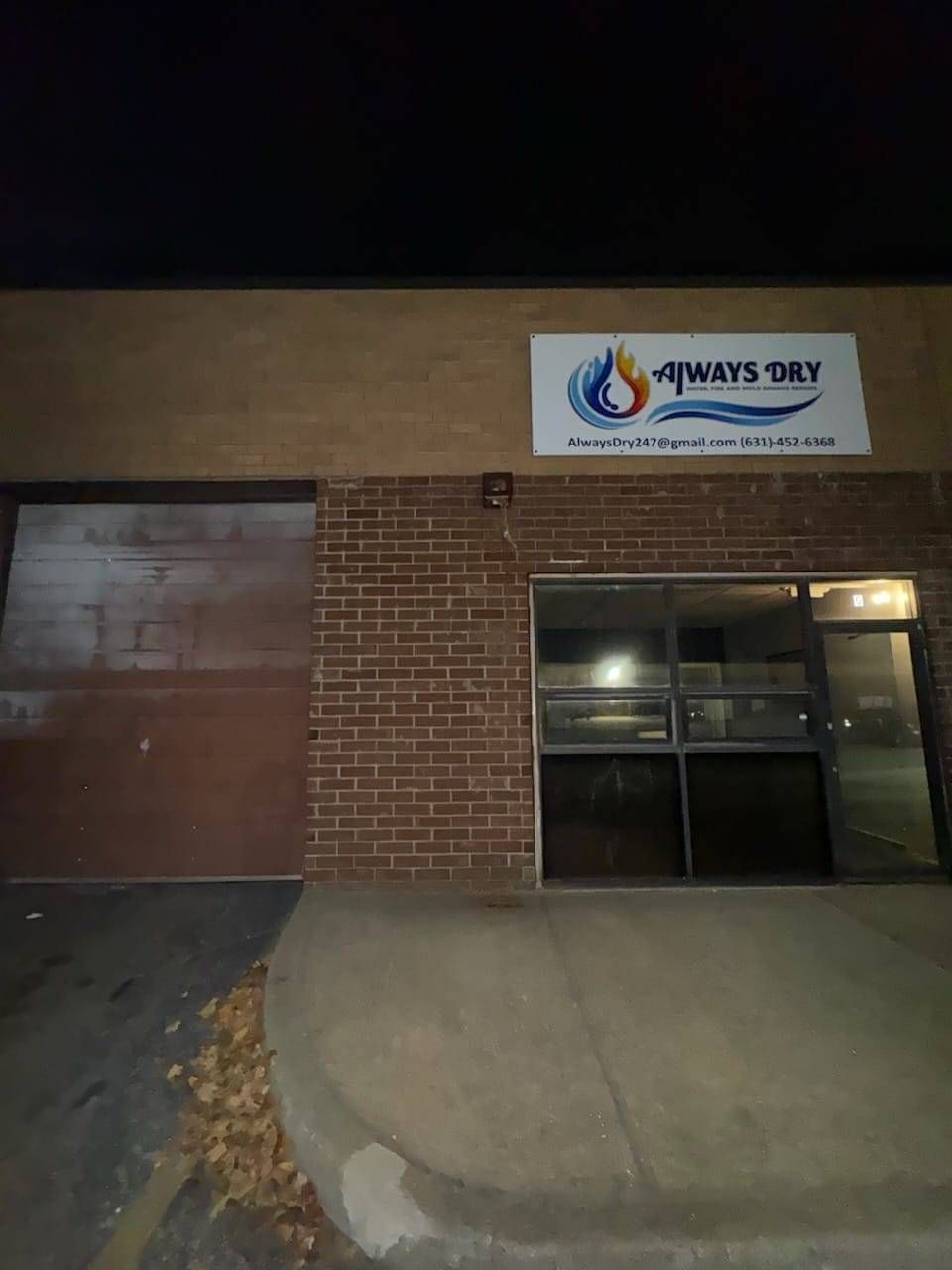 A brick building at night with a large bay door and a business sign reading 