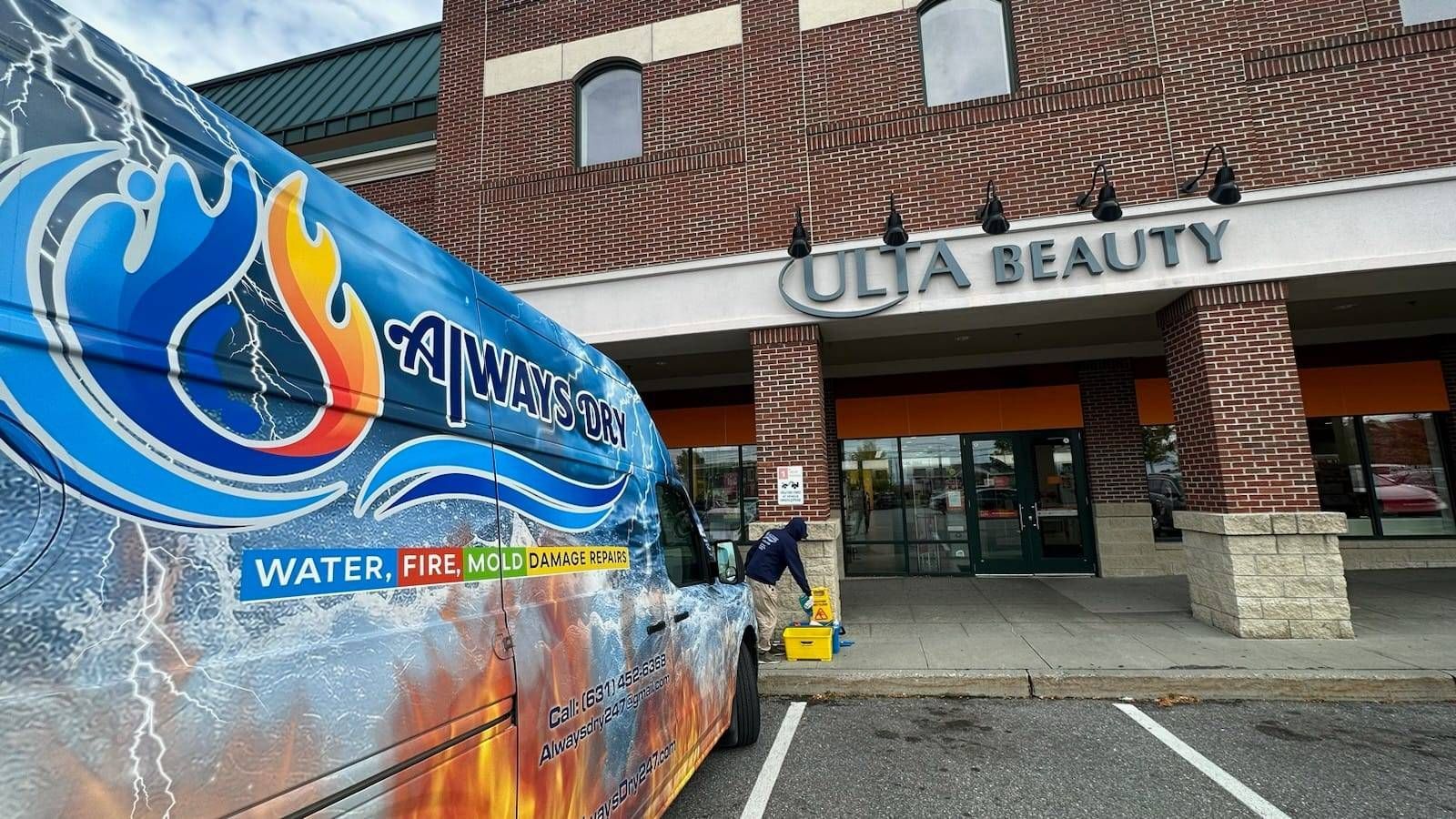 A service van with water and fire graphics parked outside an Ulta Beauty store, with a technician working near the entrance.