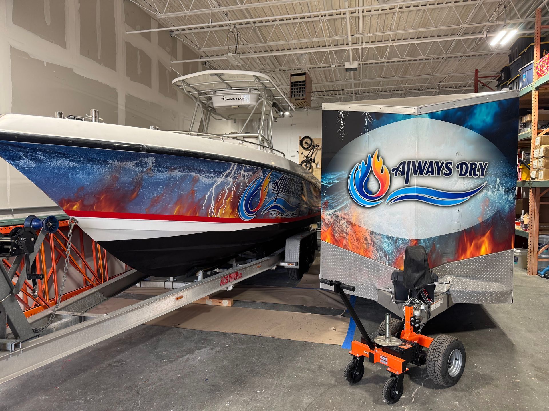 A boat with a flame and water graphic wrap on a trailer next to a branded trailer being moved by an orange electric dolly.