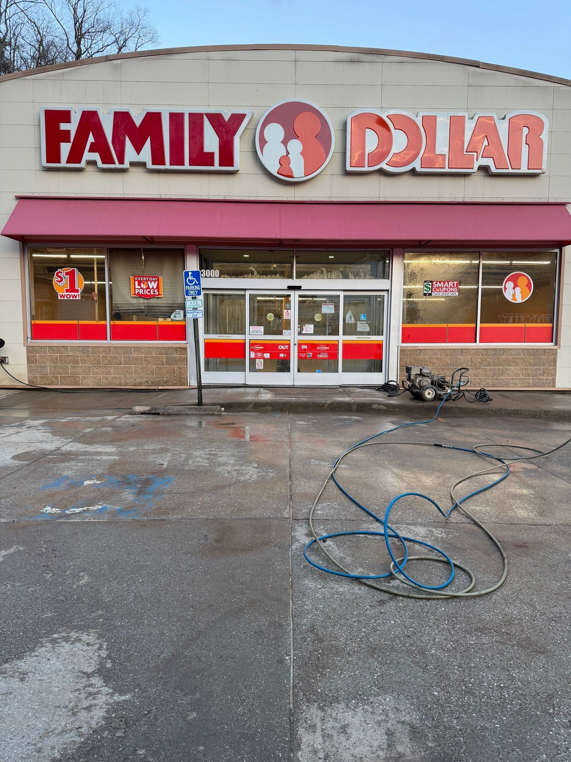 A Family Dollar store storefront with a tan facade, red awning, and a blue coiled hose on the pavement in front.