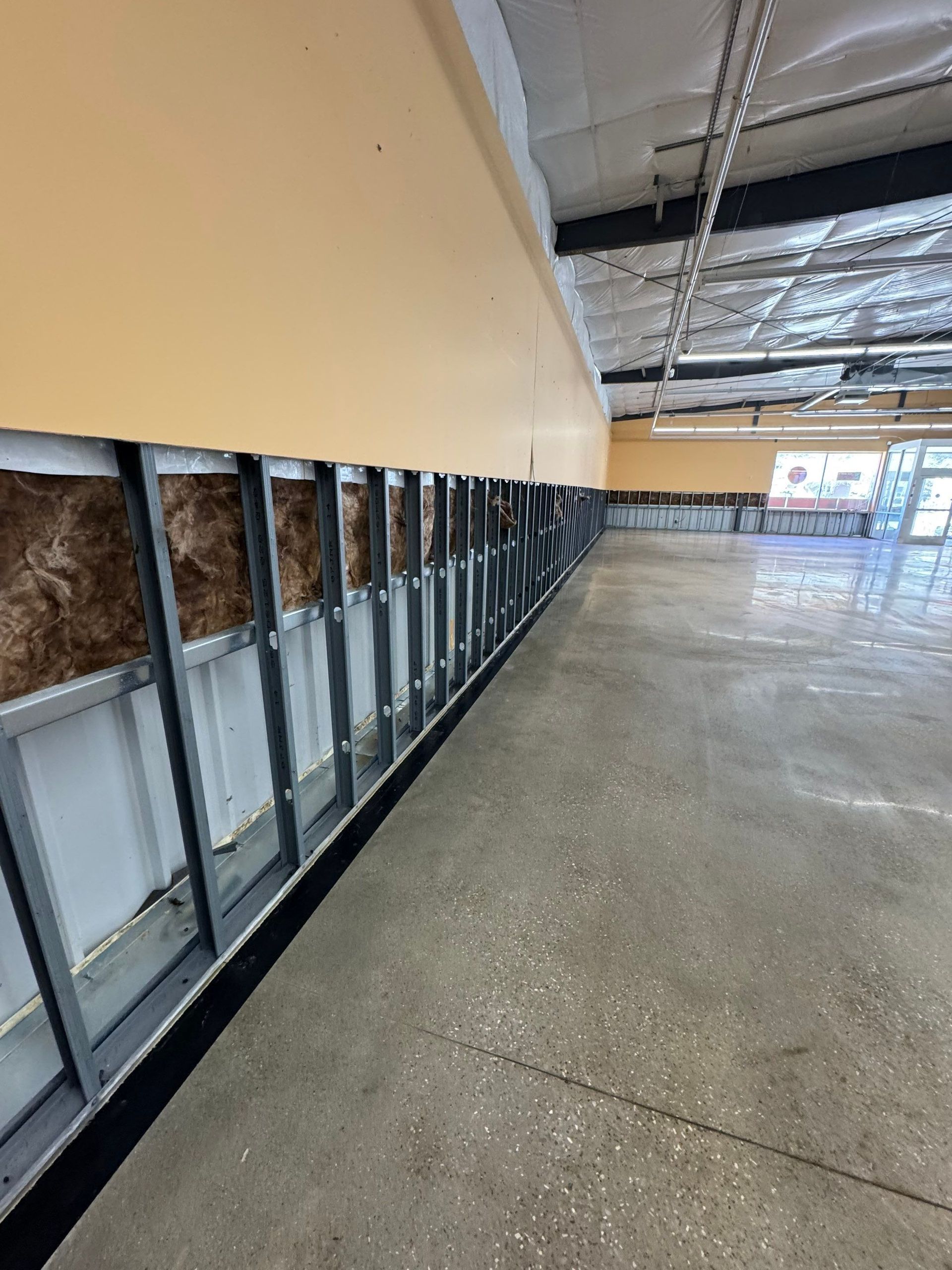 A construction site showing metal wall studs installed in front of an insulated exterior wall with a concrete floor.
