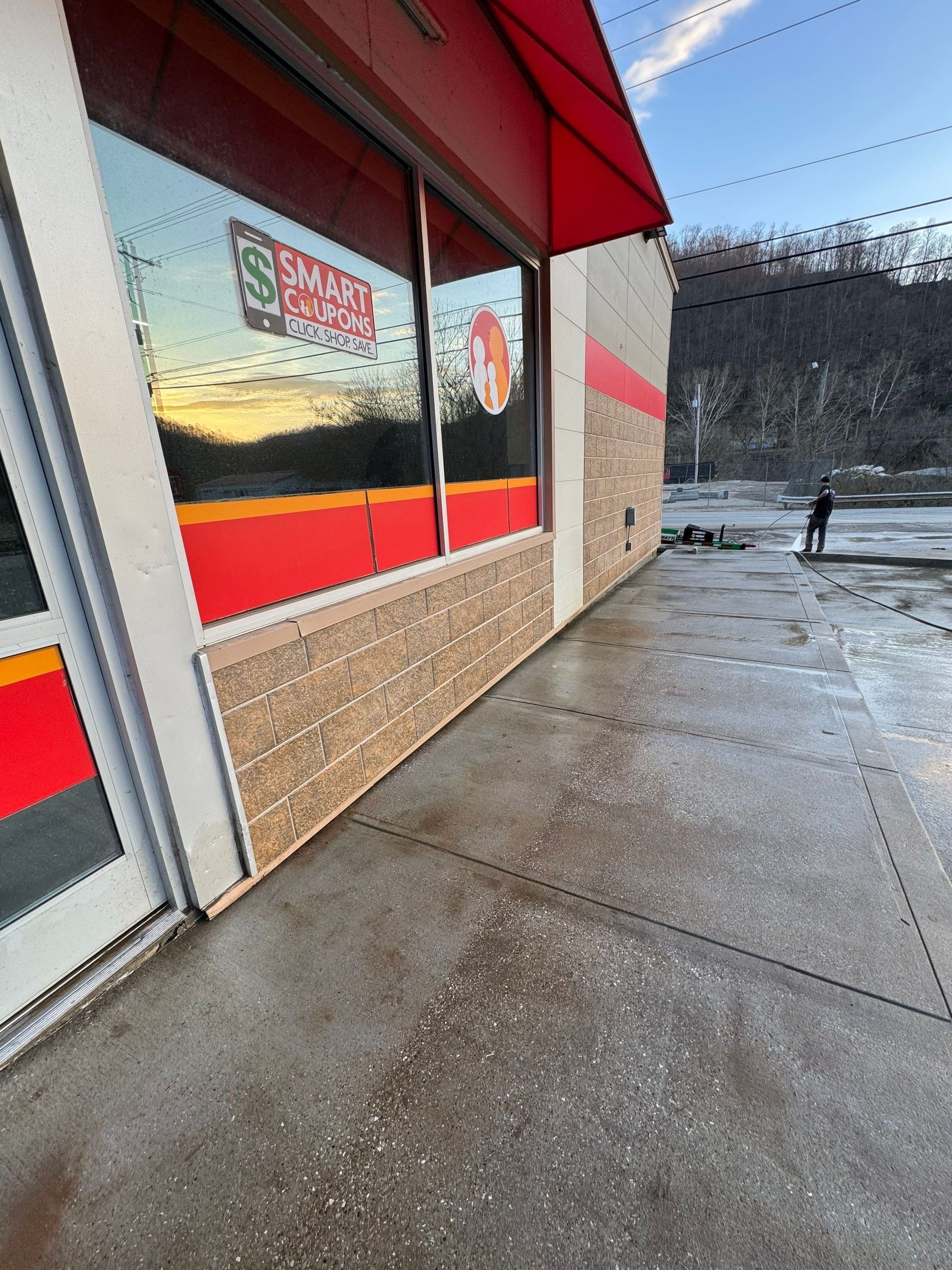 A side view of a Smart Foodservice store with brick lower walls, red trim, and a person walking in the parking lot nearby.