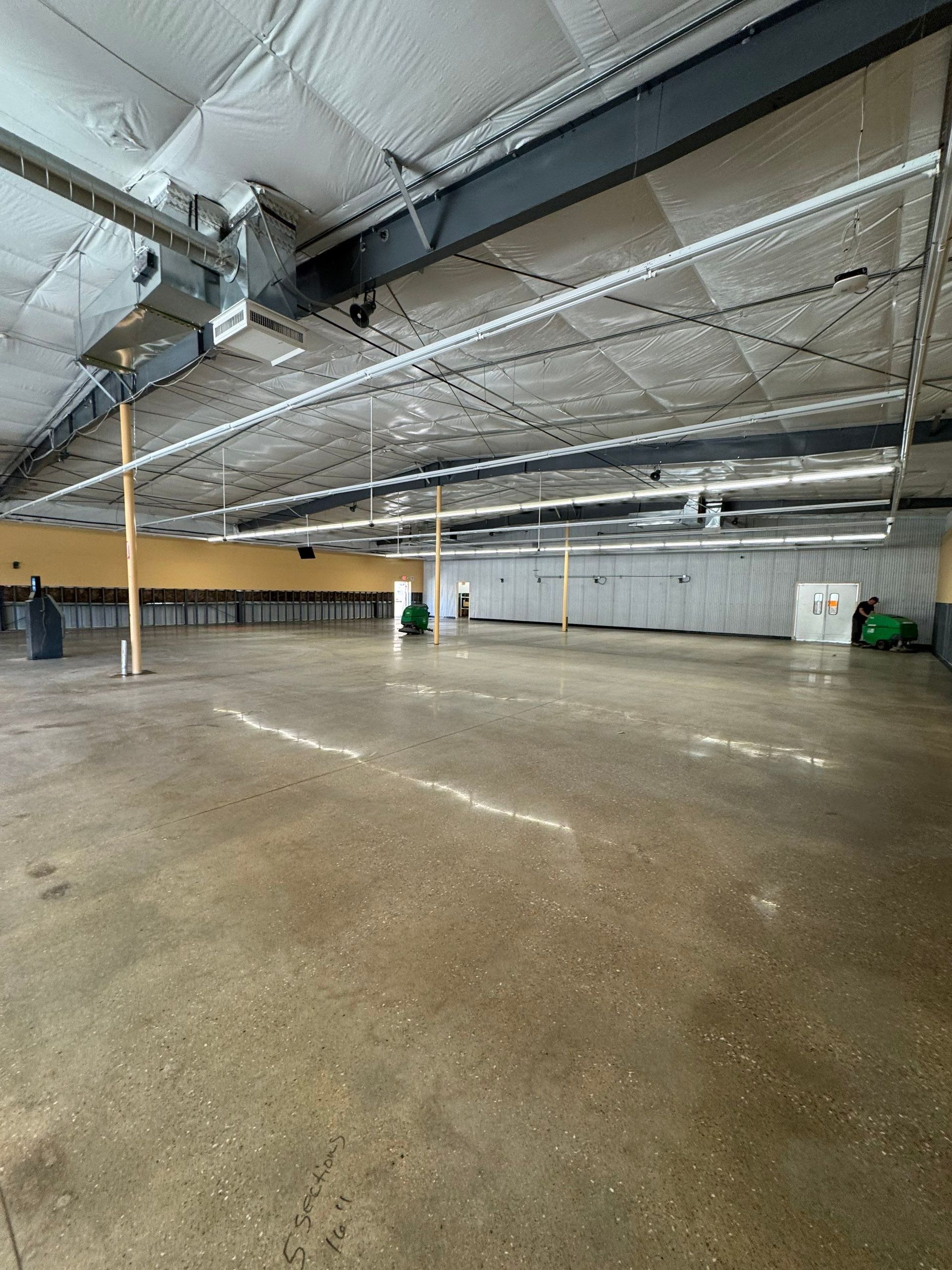A wide-angle interior view of an empty warehouse space with polished concrete floors and exposed rafters.