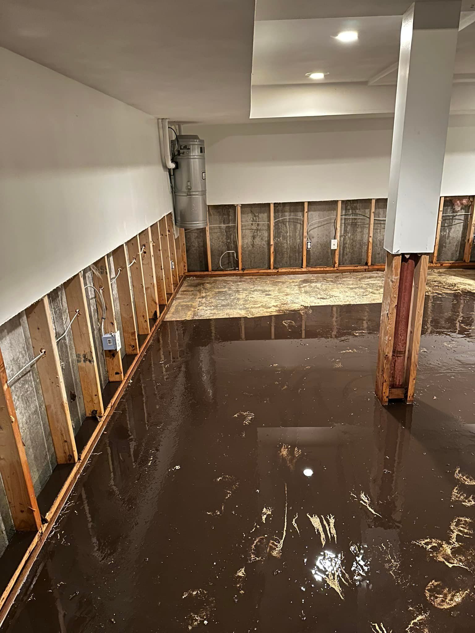 A flooded basement interior showing standing dark water against exposed wooden wall studs and a support pillar.