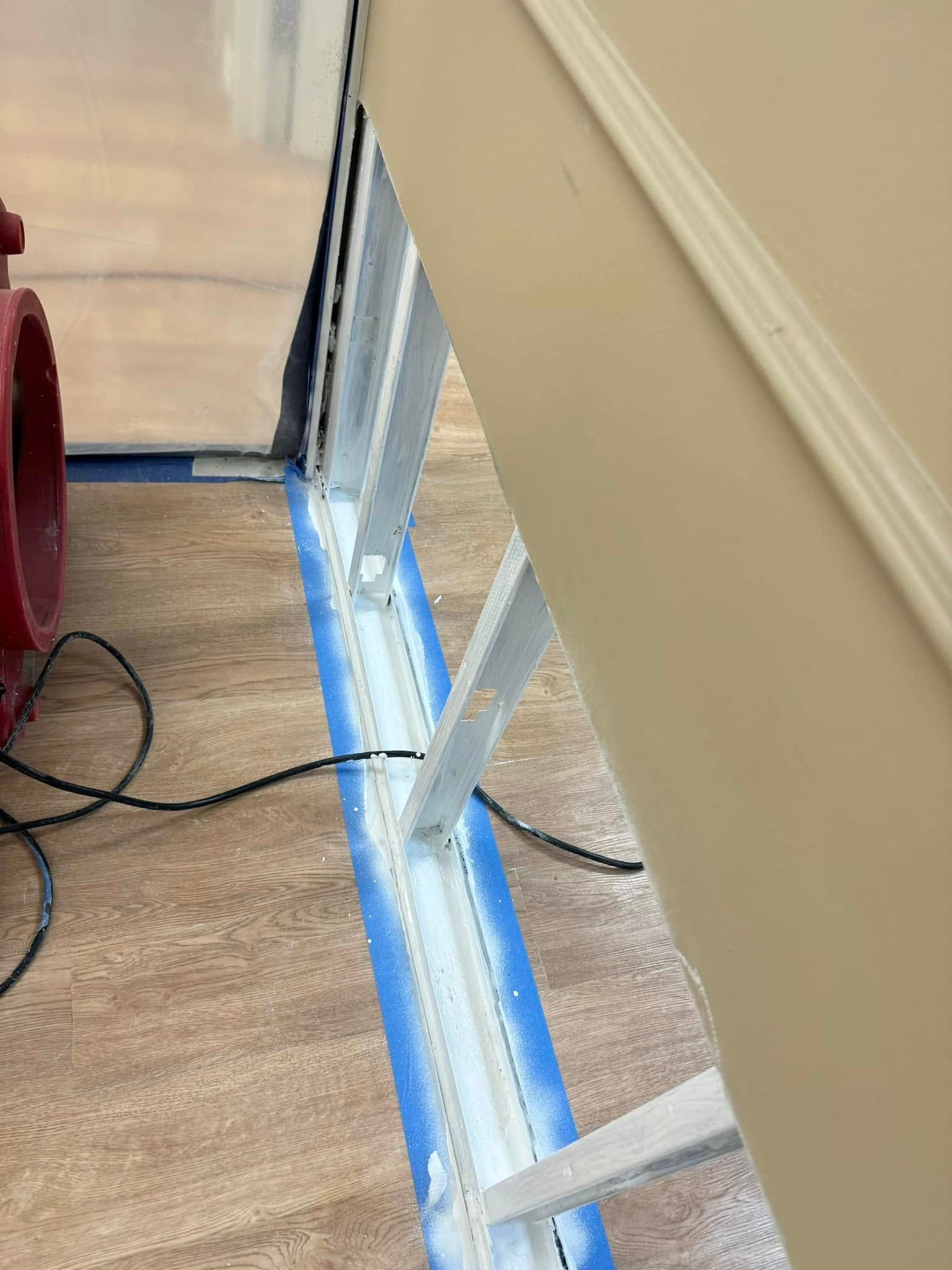 Metal wall studs are visible in an unfinished wall opening, with blue painter's tape outlining the floor and wall edges.