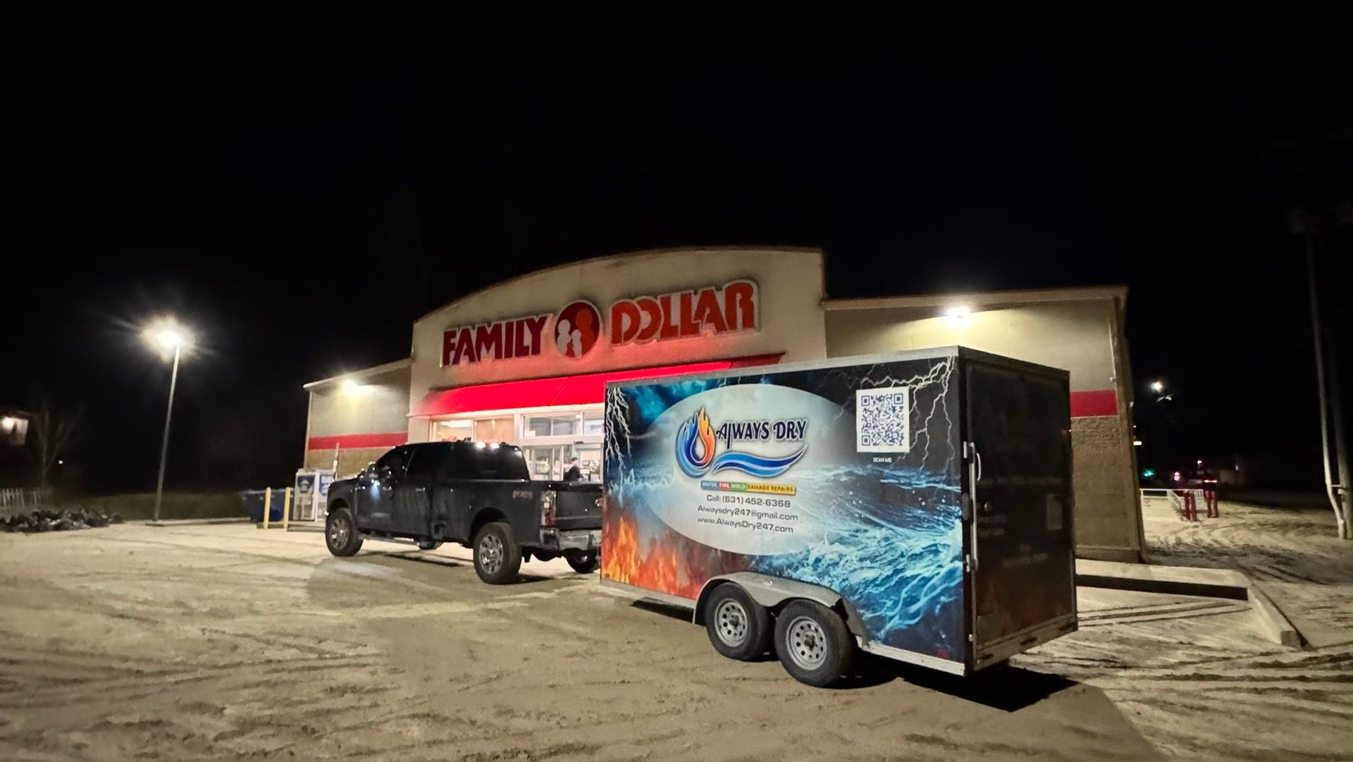 A dark pickup truck pulling a branded trailer parked in front of a Family Dollar store at night.